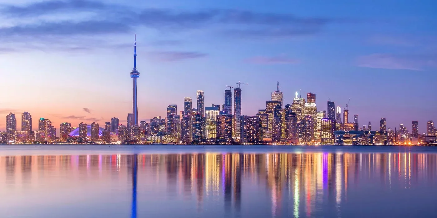 Skyline of Toronto cityscape at dusk with reflections on the water in the foreground.