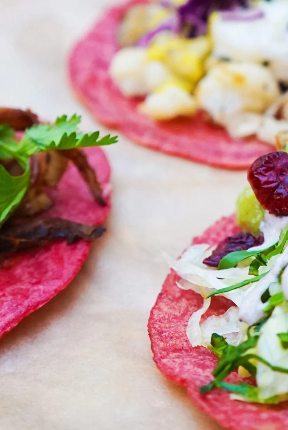 Close-up of colorful open-faced tacos with various ingredients on pink corn tortillas.