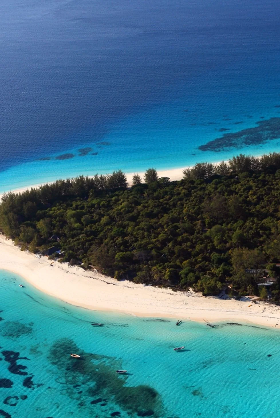 Aerial view of a tropical beach with white sand, clear turquoise water, and a forested shoreline.