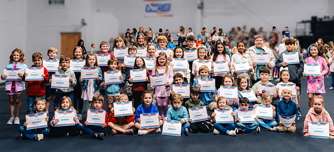Group of children holding certificates for kindness inside a large indoor facility