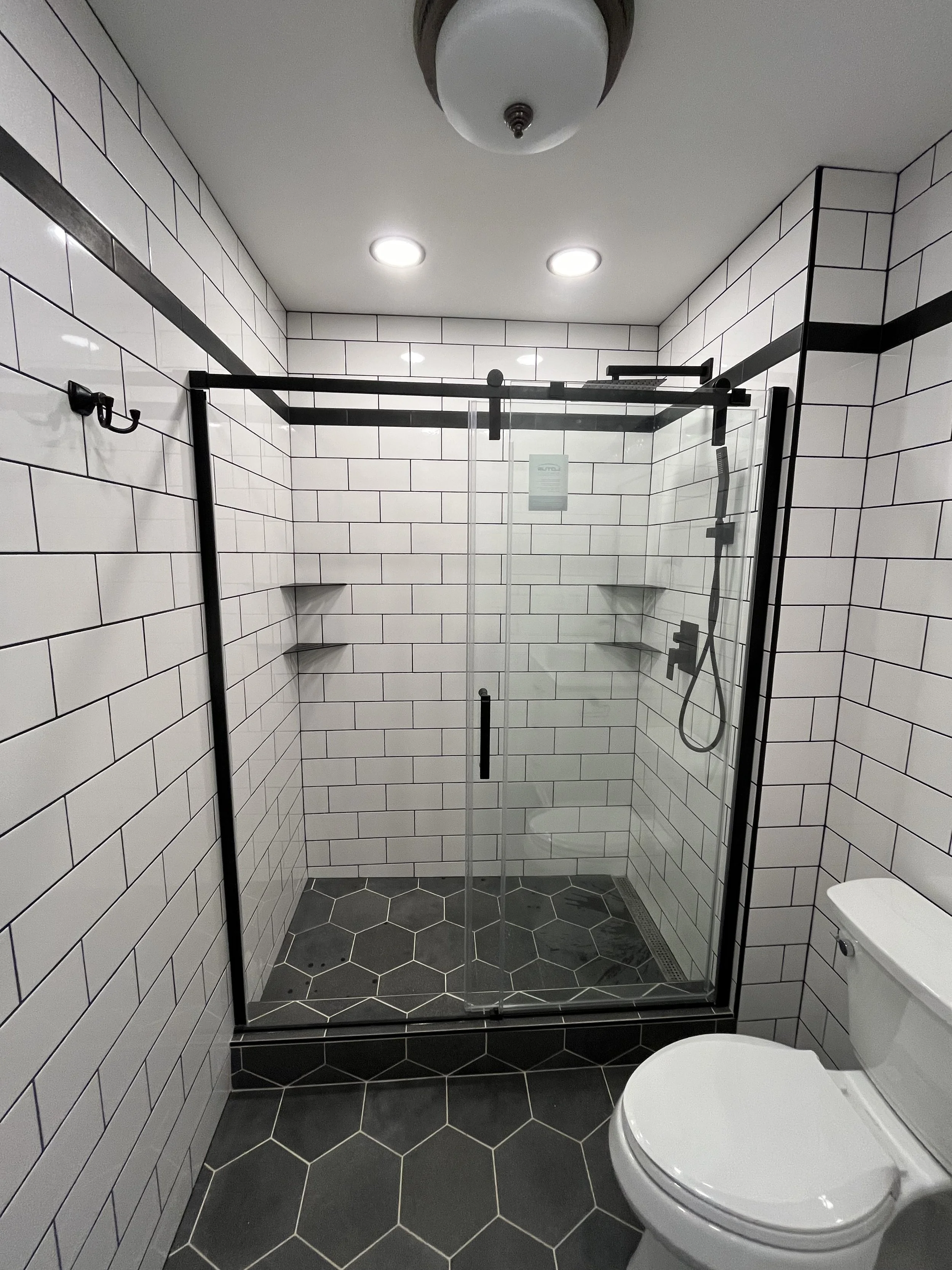 Modern bathroom with white subway tiles on the walls, black grout lines, black hexagonal floor tiles, a glass shower door, and a white toilet.