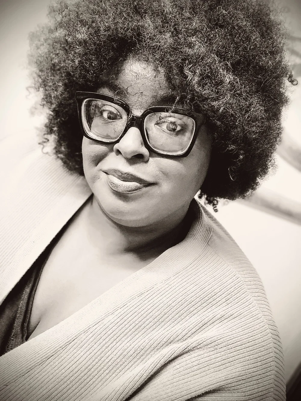 A woman with curly hair and glasses looking at the camera, smiling slightly, in black and white.