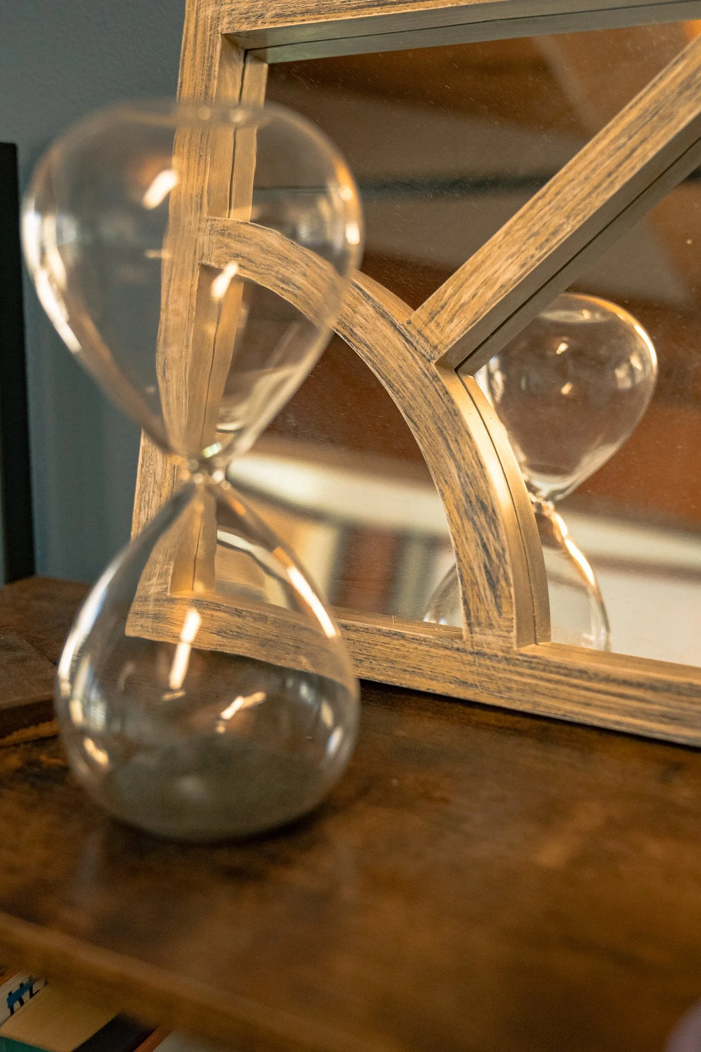 A wooden table with a mirror and an hourglass in front of it, reflecting the hourglass in the mirror.