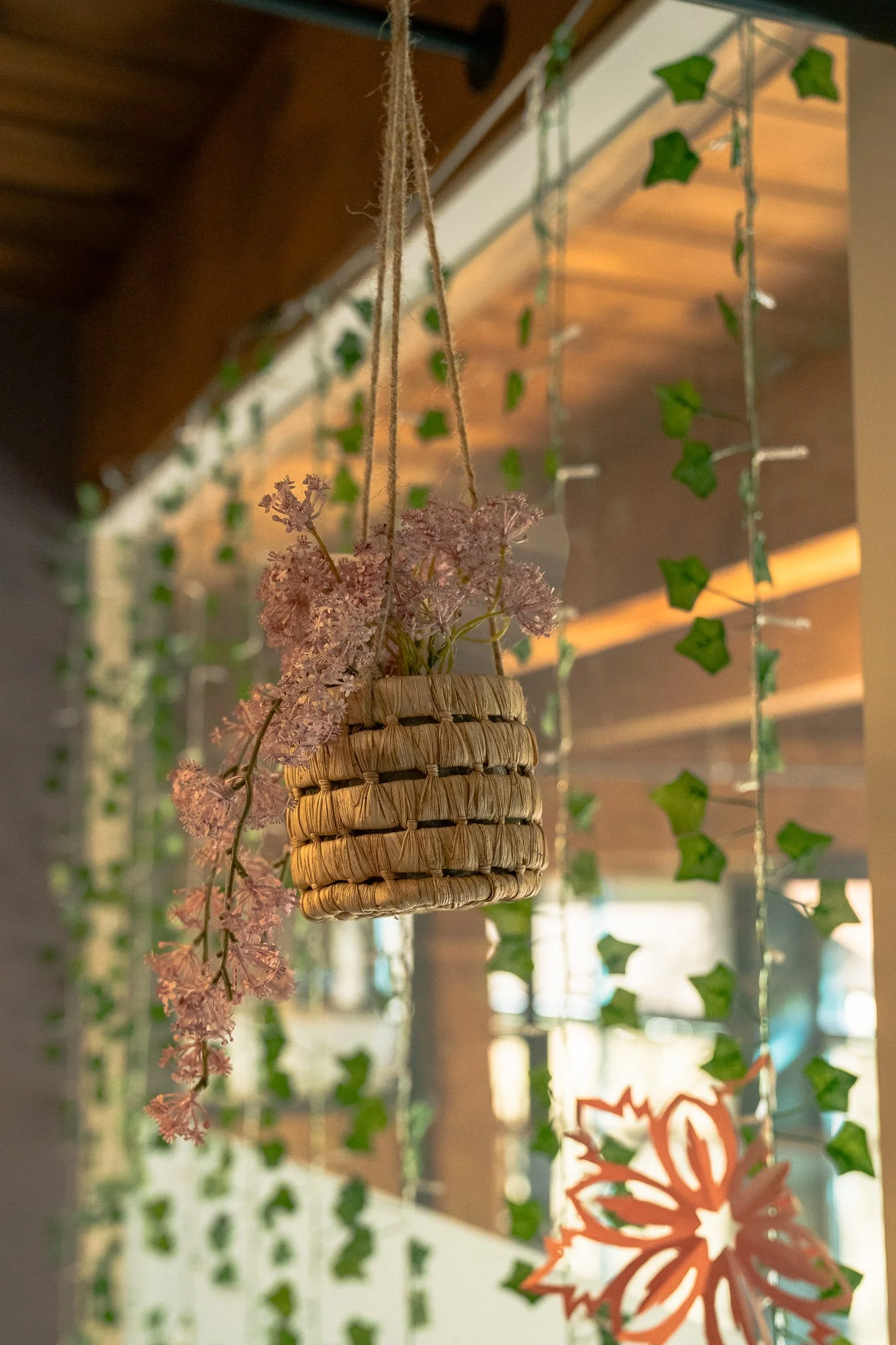 Hanging woven basket with pink flowers, decorated with green ivy and red paper snowflake decorations in the background.