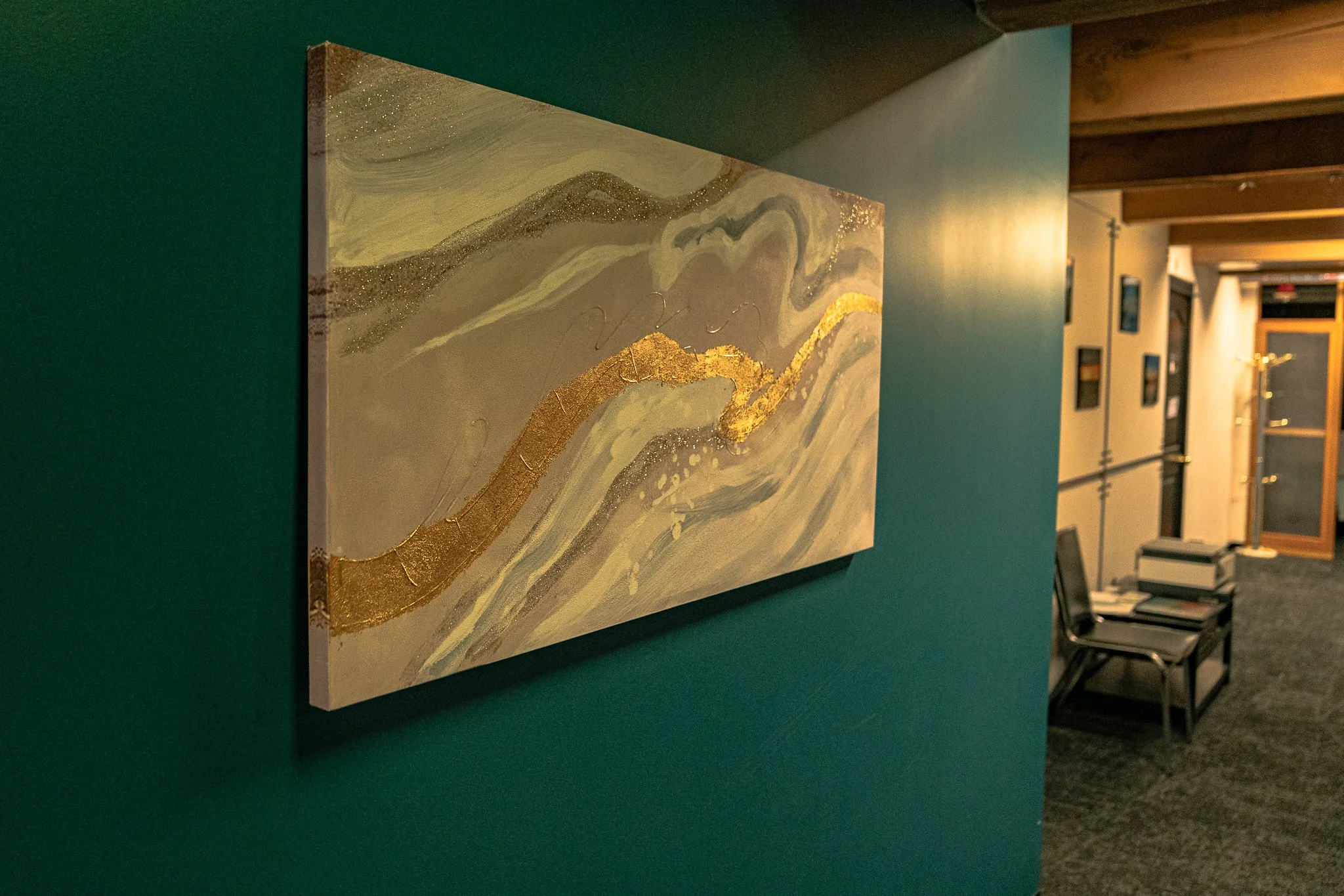 Abstract landscape painting with gold, gray, and cream colors on a green wall in an art gallery or waiting area.