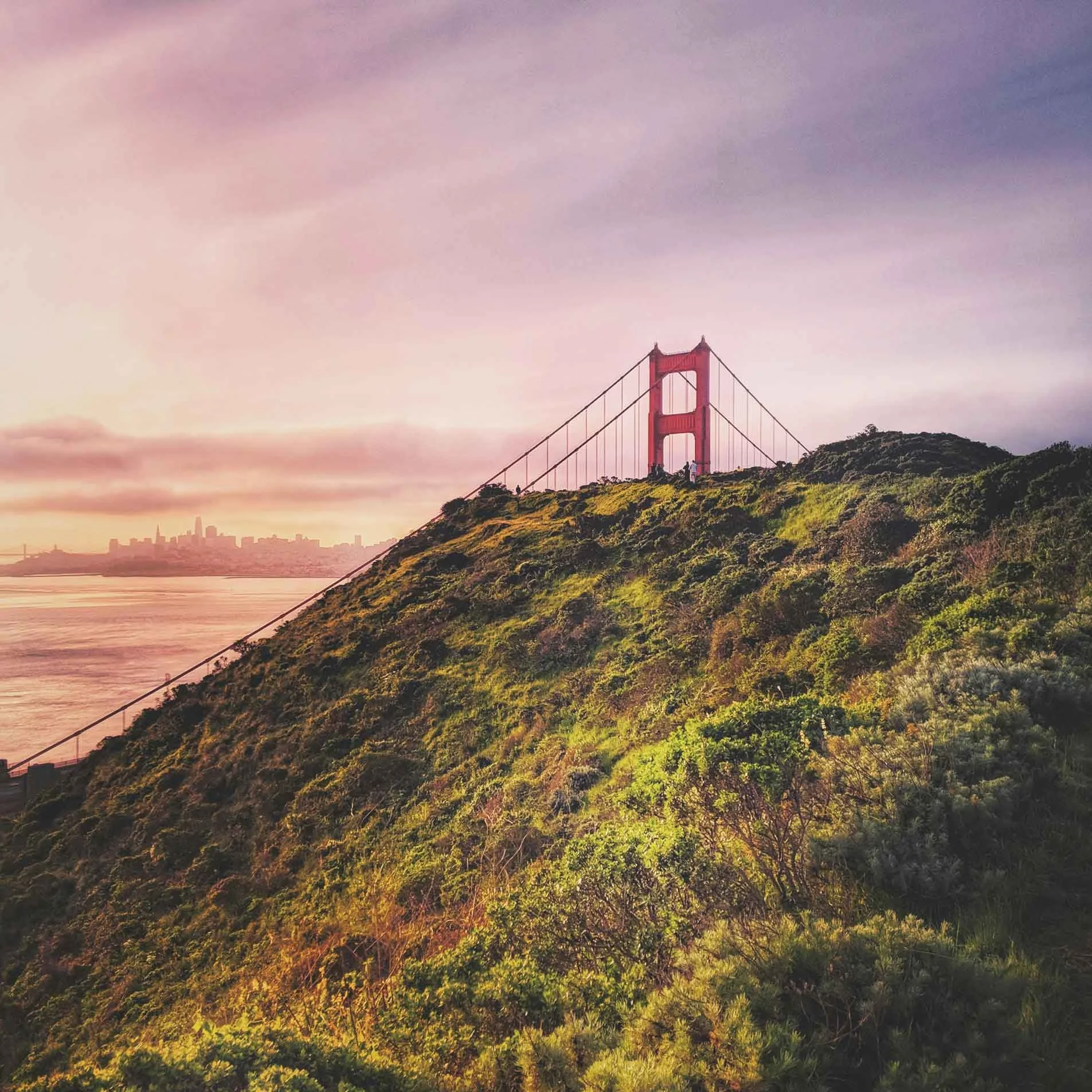 Golden Gate Bridge viewed over a green hill at sunset with the San Francisco city skyline in the distance. San Francisco is where Yvette Fama offers somatic therapy, sex therapy, and EMDR therapy to individuals and couples.