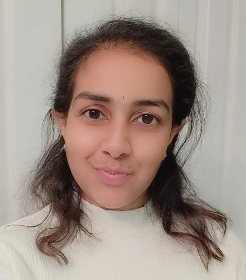 A woman with dark brown hair and a light complexion taking a selfie in front of a plain door, wearing a white sweater.