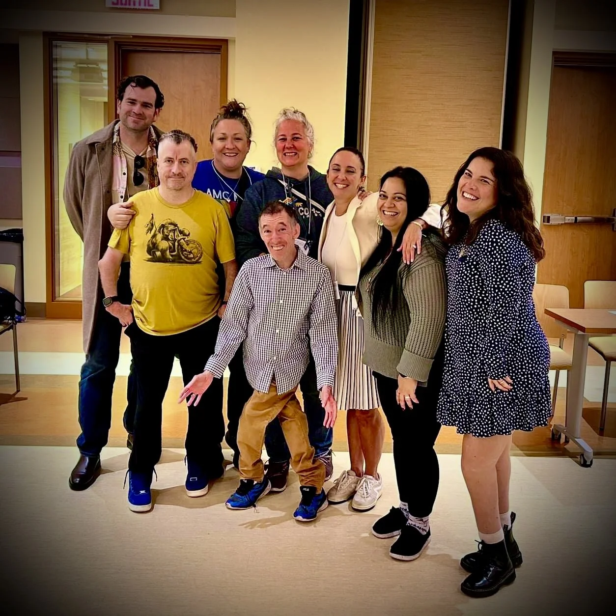 Group of nine smiling people posing together indoors at a casual event.