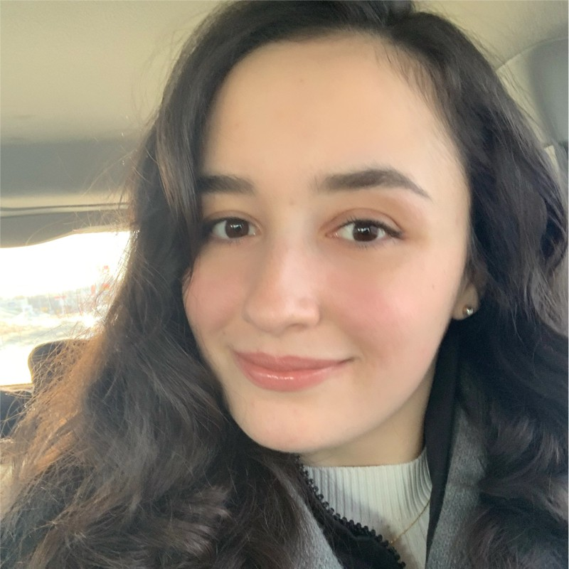 Young woman with long dark wavy hair smiling inside a car.