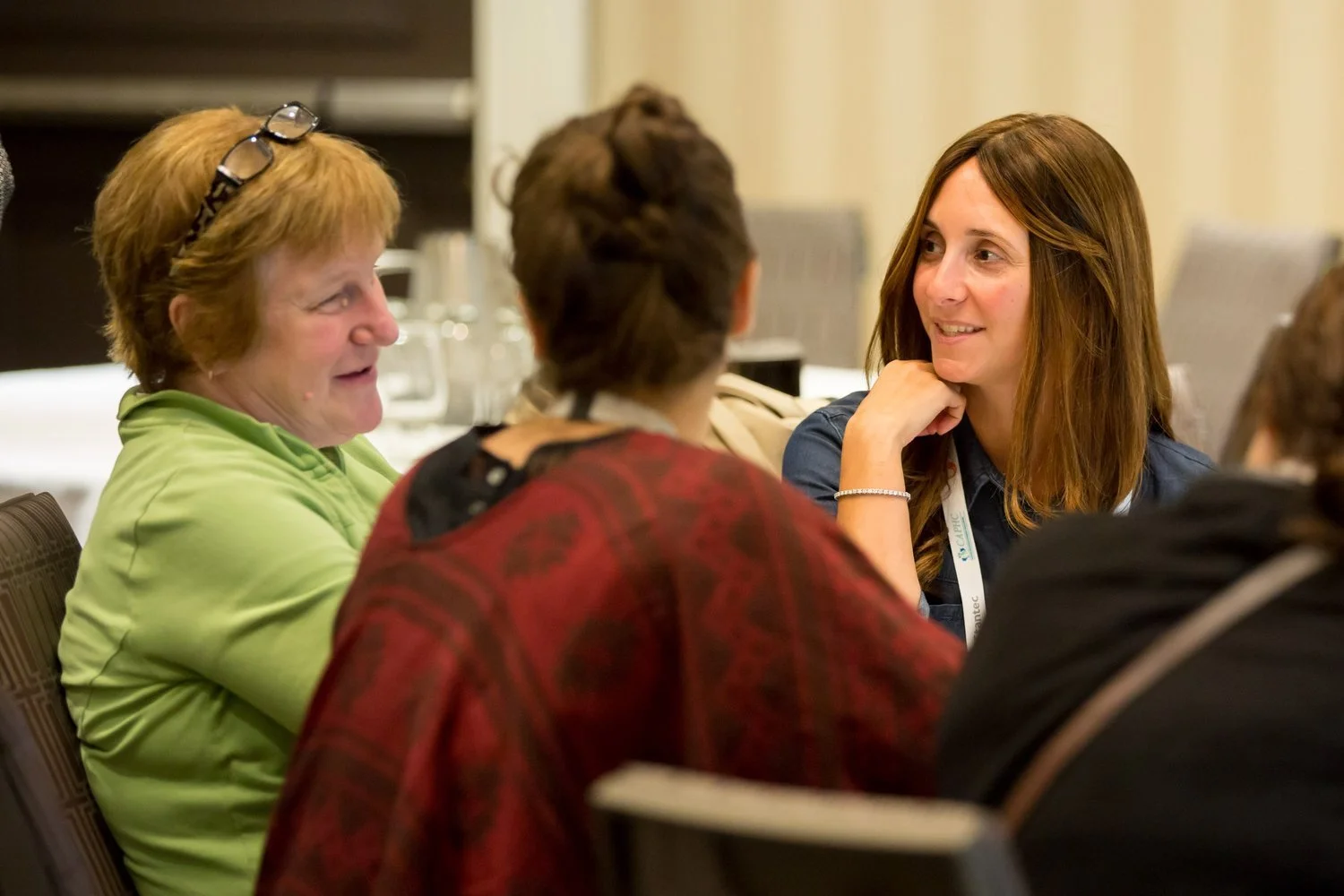 Group of women sitting and talking at a conference or meeting, engaging in conversation.