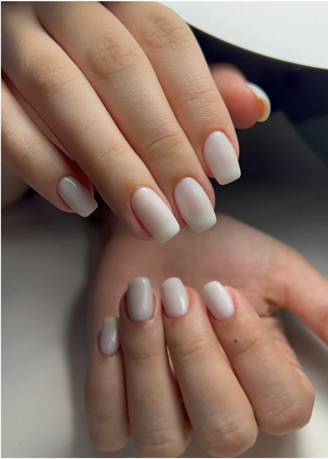 Close-up of hands with manicured nails painted in white and light gray colors.