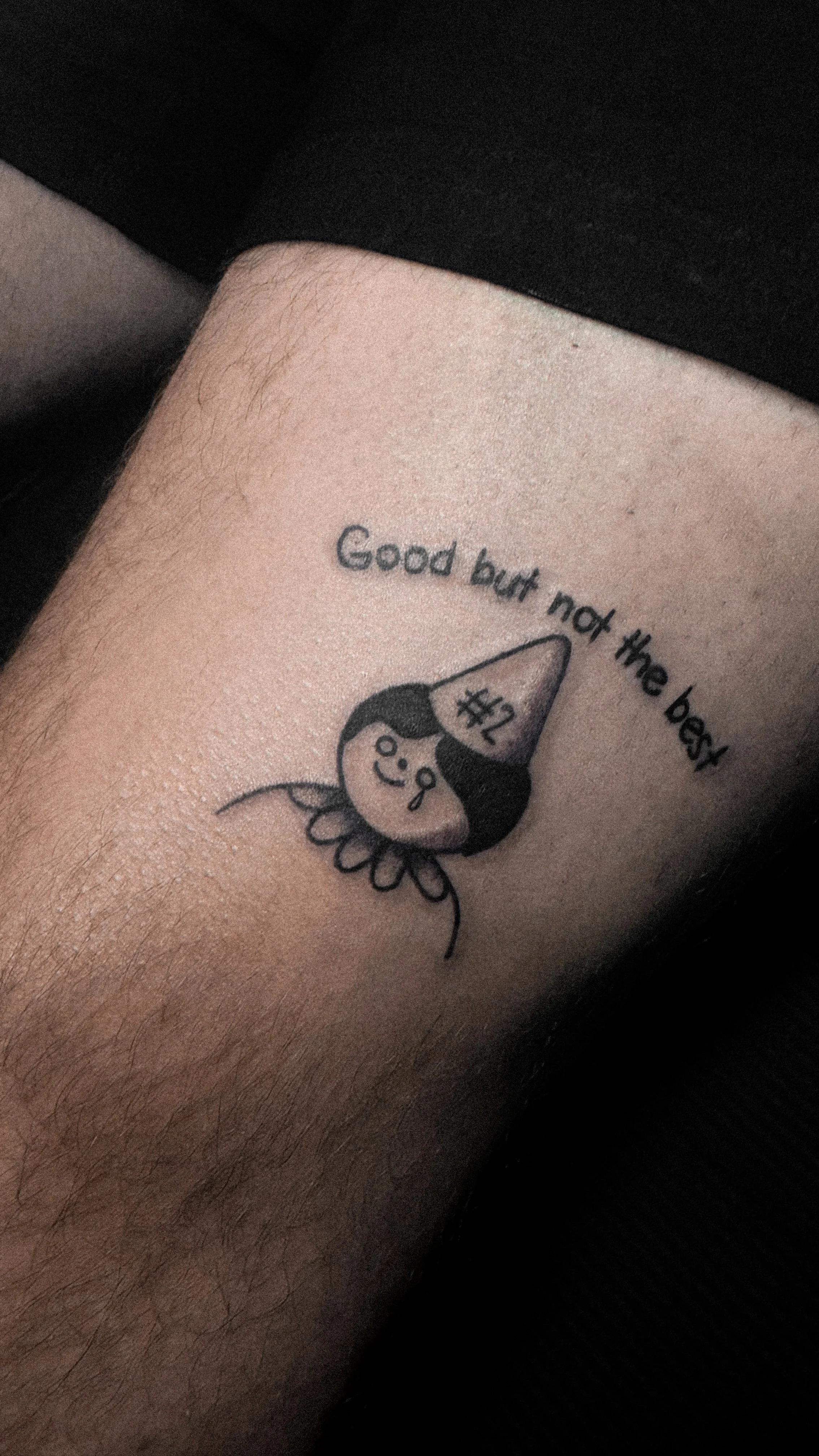 A tattoo of a cartoon girl wearing sunglasses and a party hat that reads '#1', with the text 'Good but not the best' above it.