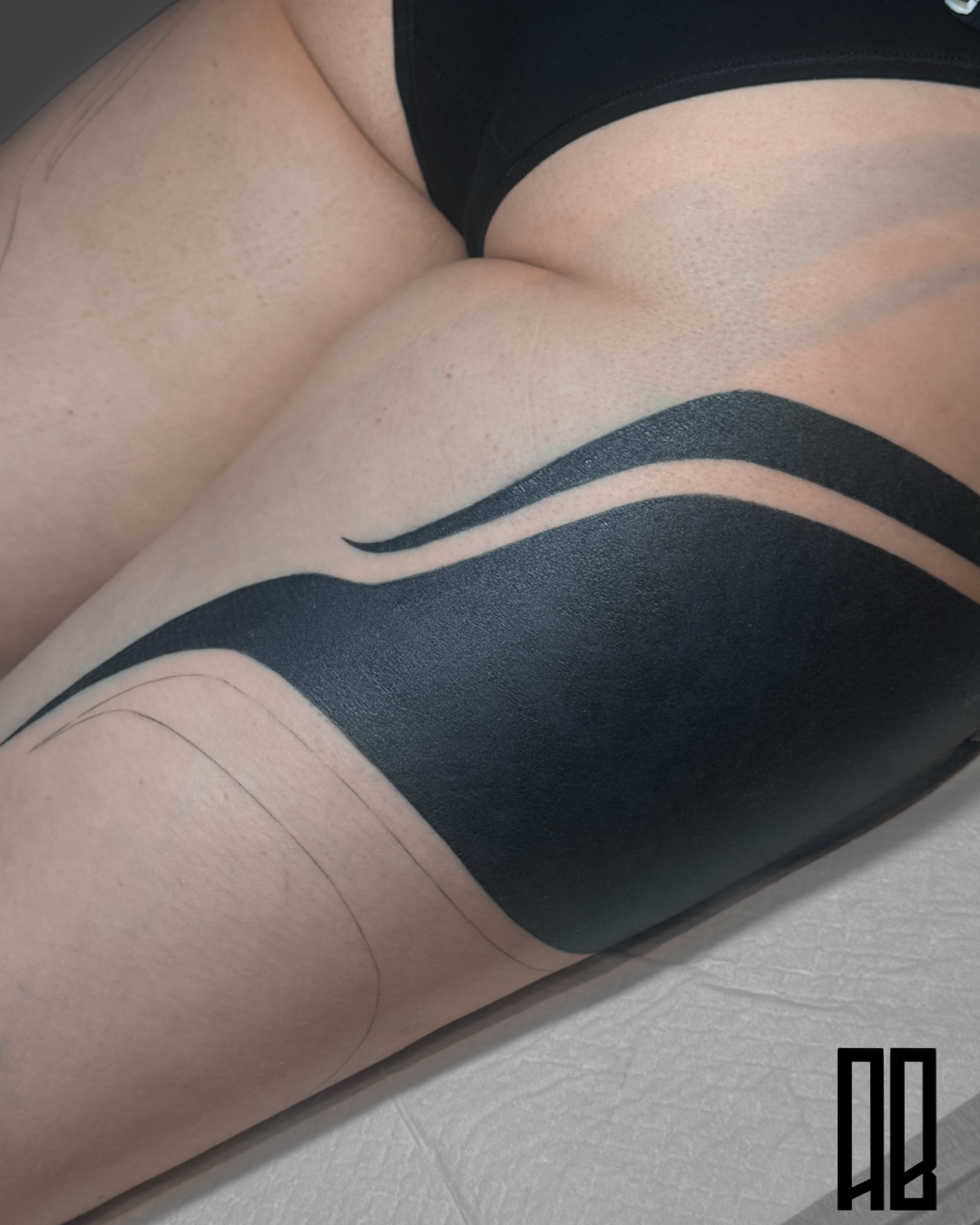 Close-up of a person's thigh with black abstract tattoo and black shorts, with some dotted skin texture visible.