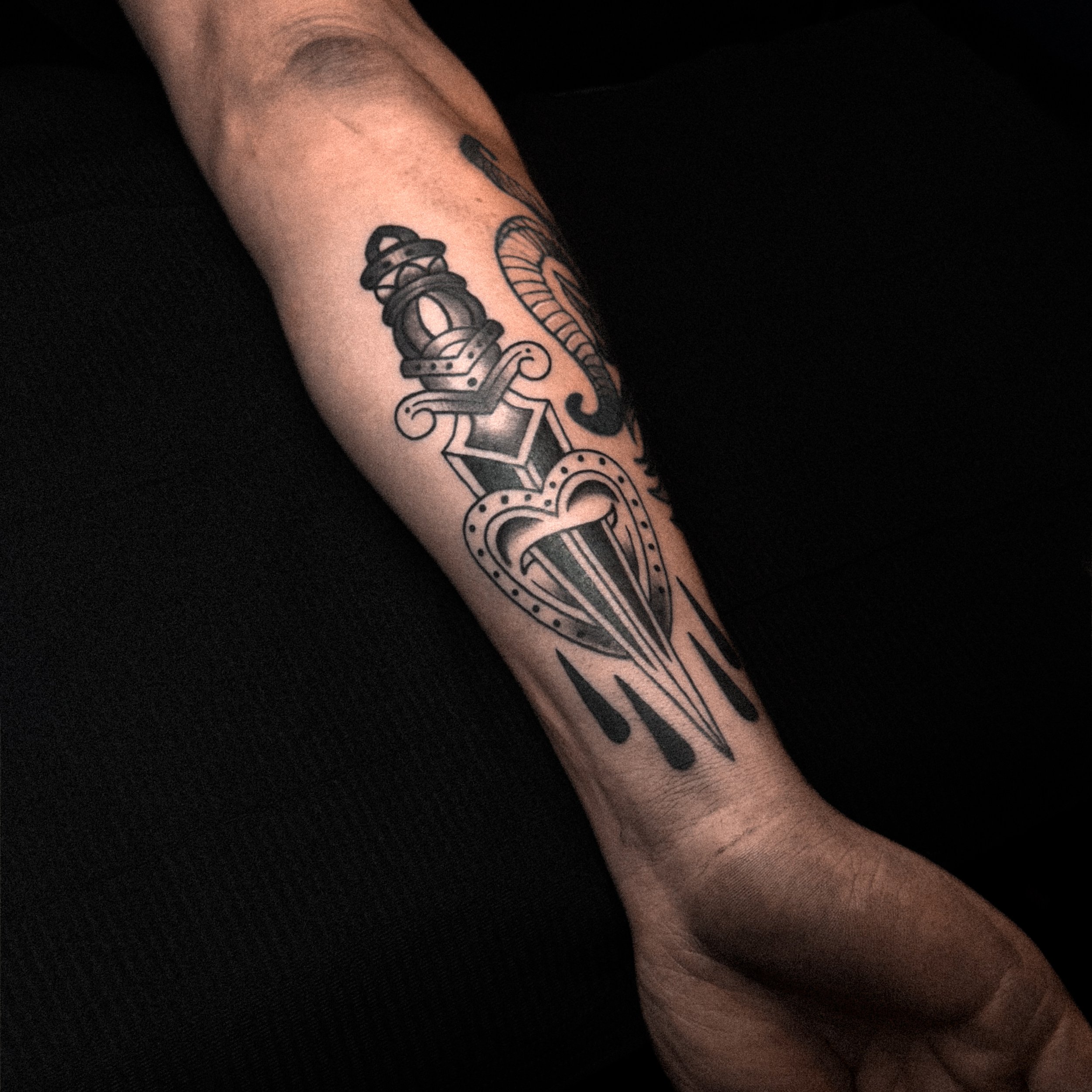 Tattoo of a dagger piercing a heart on a person's forearm.