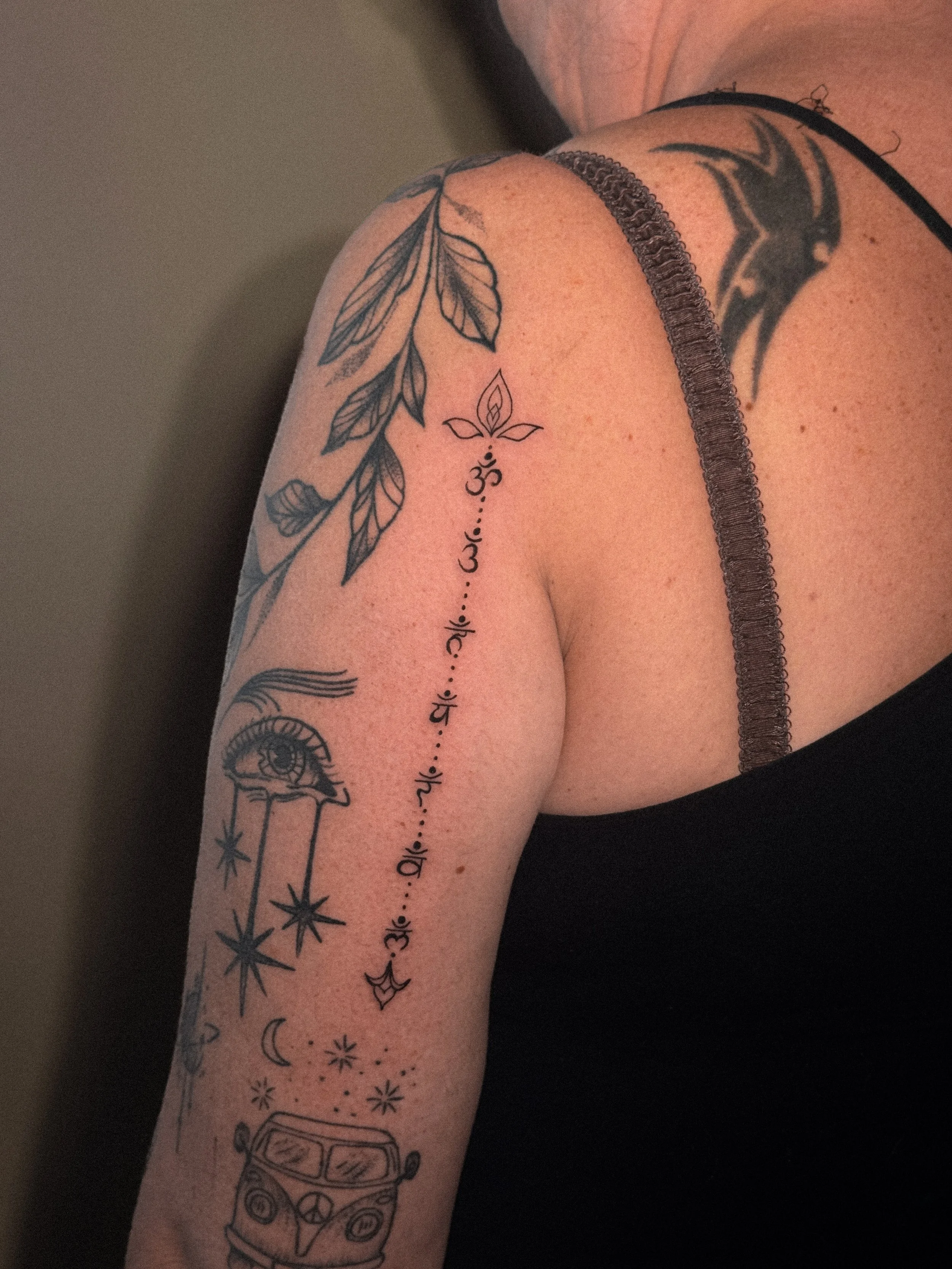 Tattoo sleeve on a person's arm featuring a leaf design, an eye with tears, stars, moons, a diamond, a van, and symbols including Om and a lotus flower.