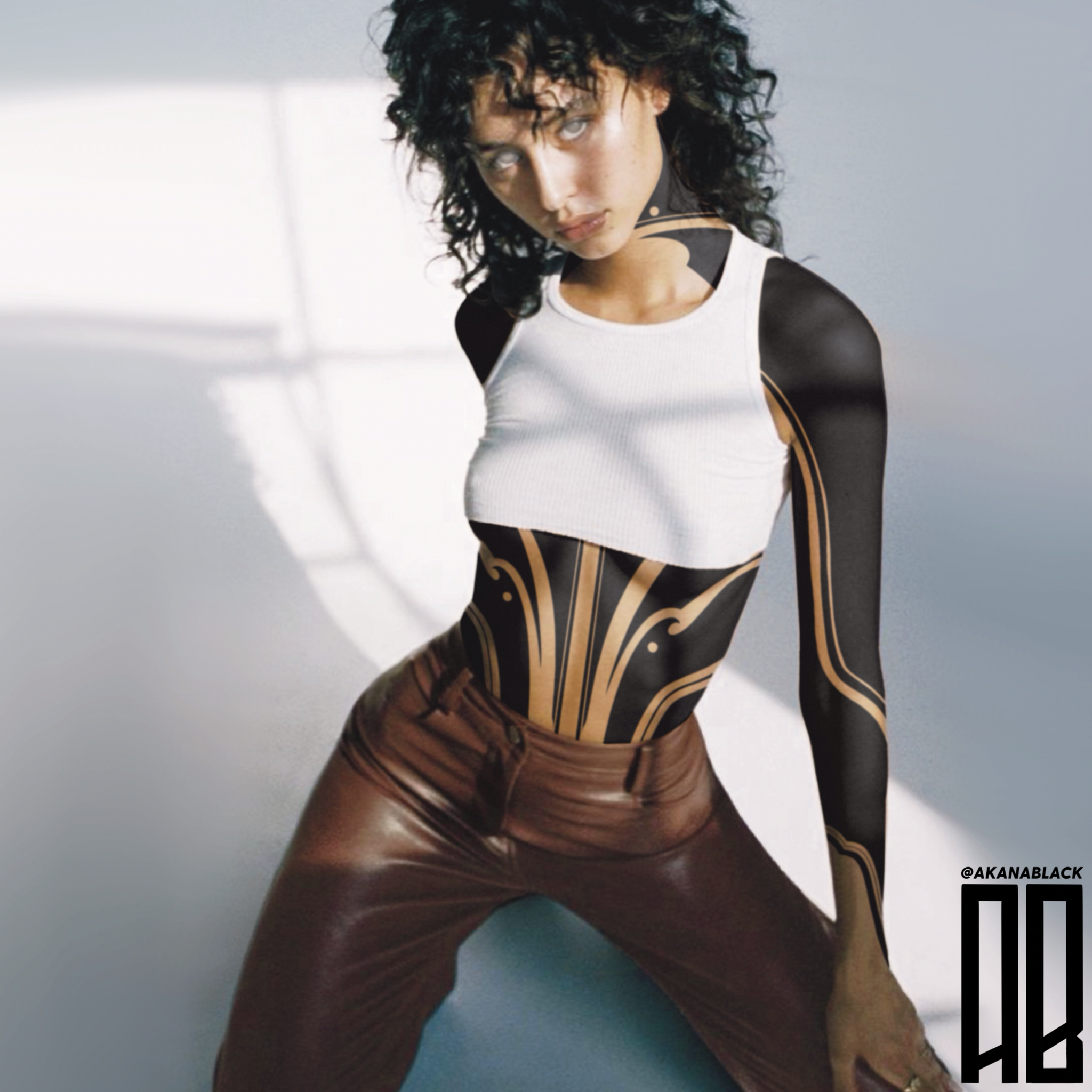 Young woman with curly black hair, wearing a sleeveless white crop top and brown leather pants, poses in front of a plain background.