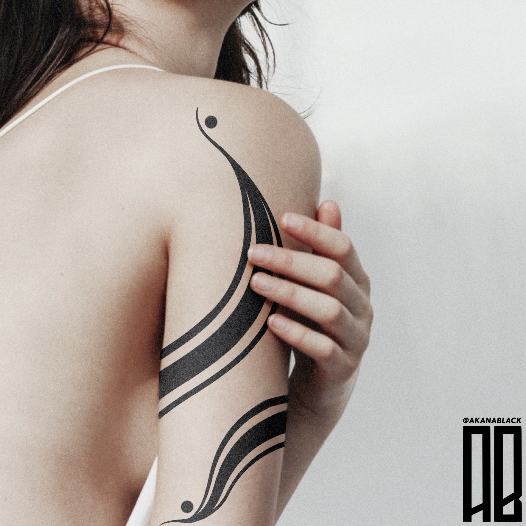 A woman with a black abstract tattoo on her shoulder and arm, partially obscured and holding her shoulder with her hand.