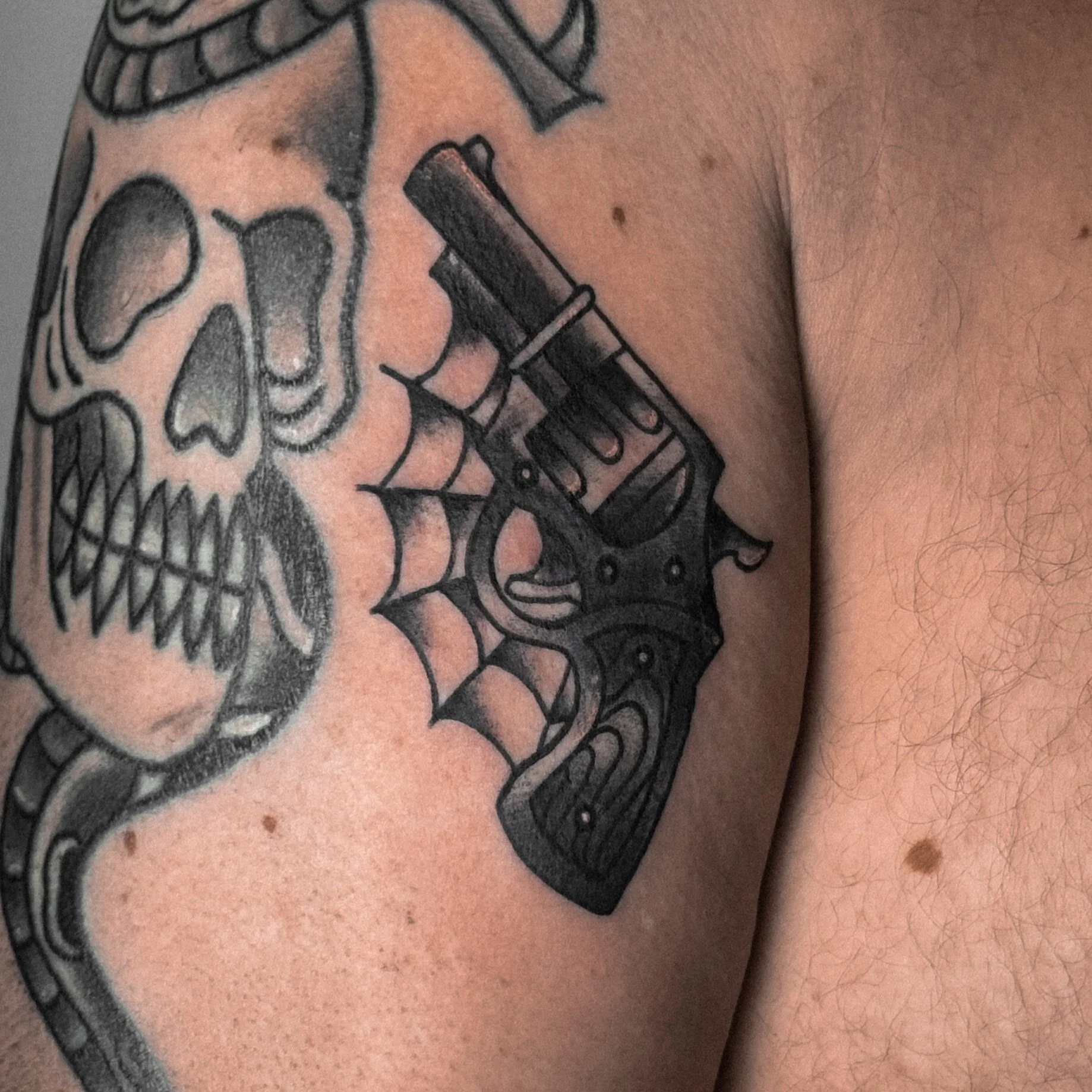 Tattoo of a skull and a handgun with spider web design.