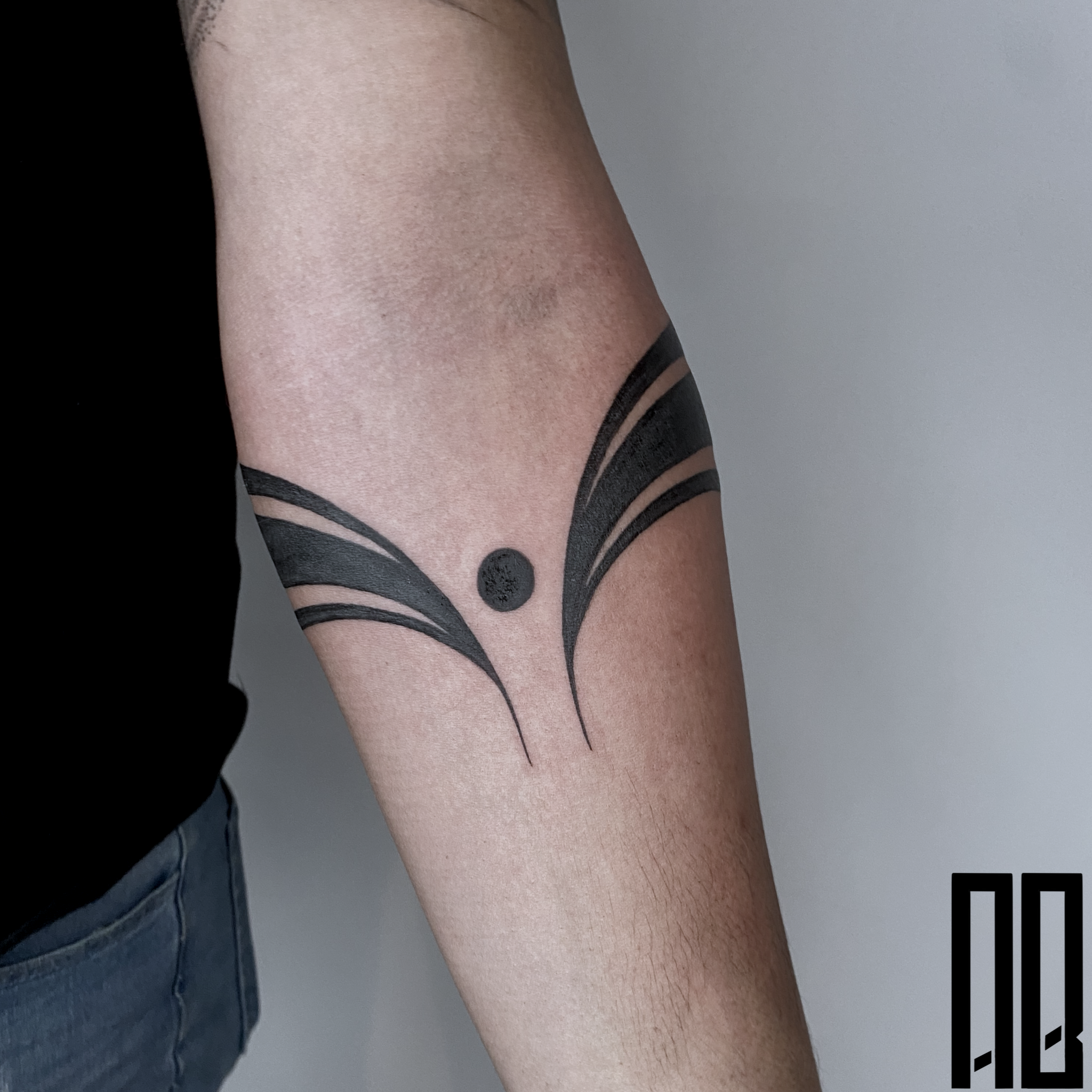 Black tattoo of abstract butterfly wings and a dot on person's arm.