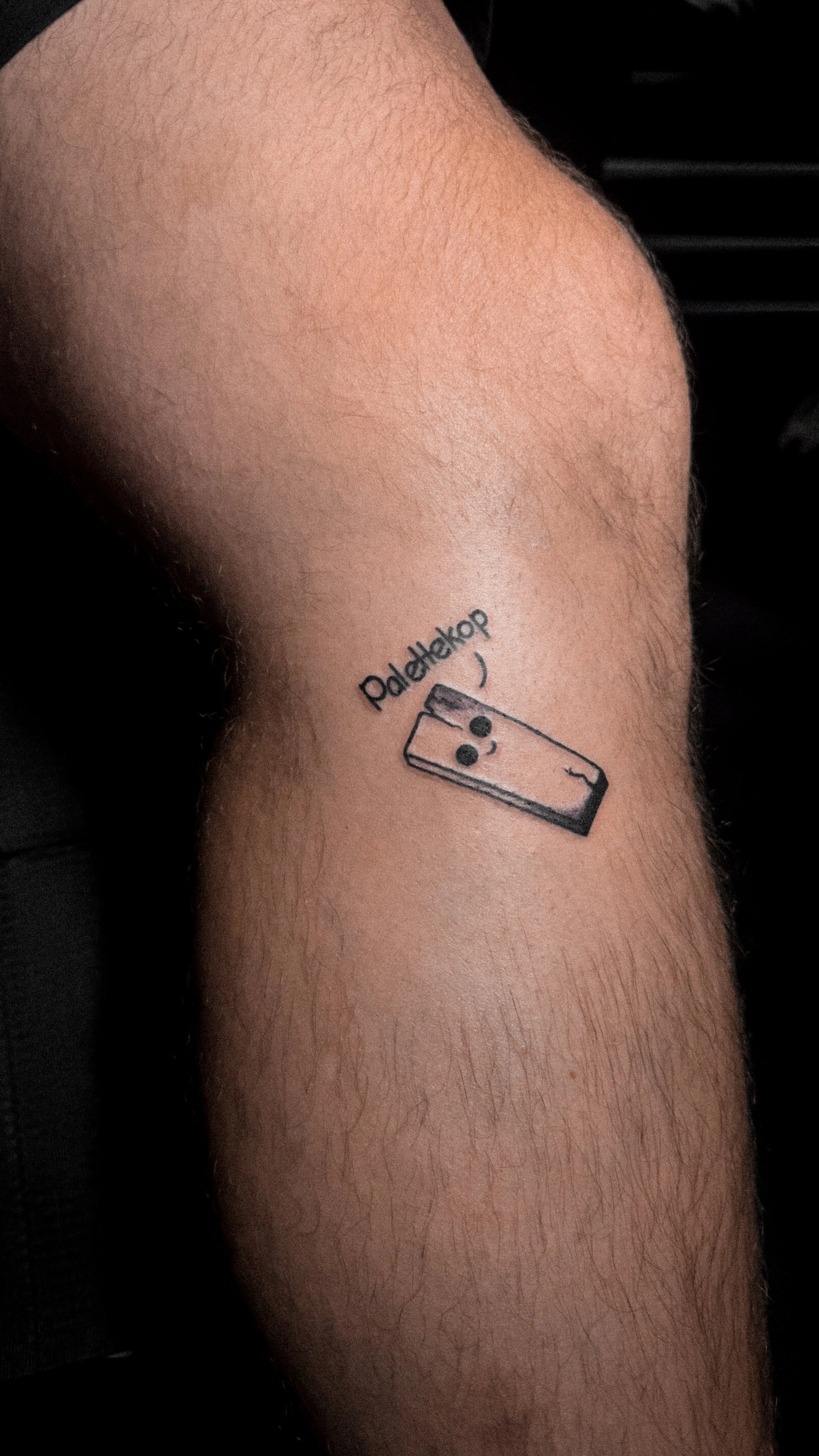Tattoo of a happy cartoon matchstick with the word 'PadleHekop' in a playful font above it on a person's calf.