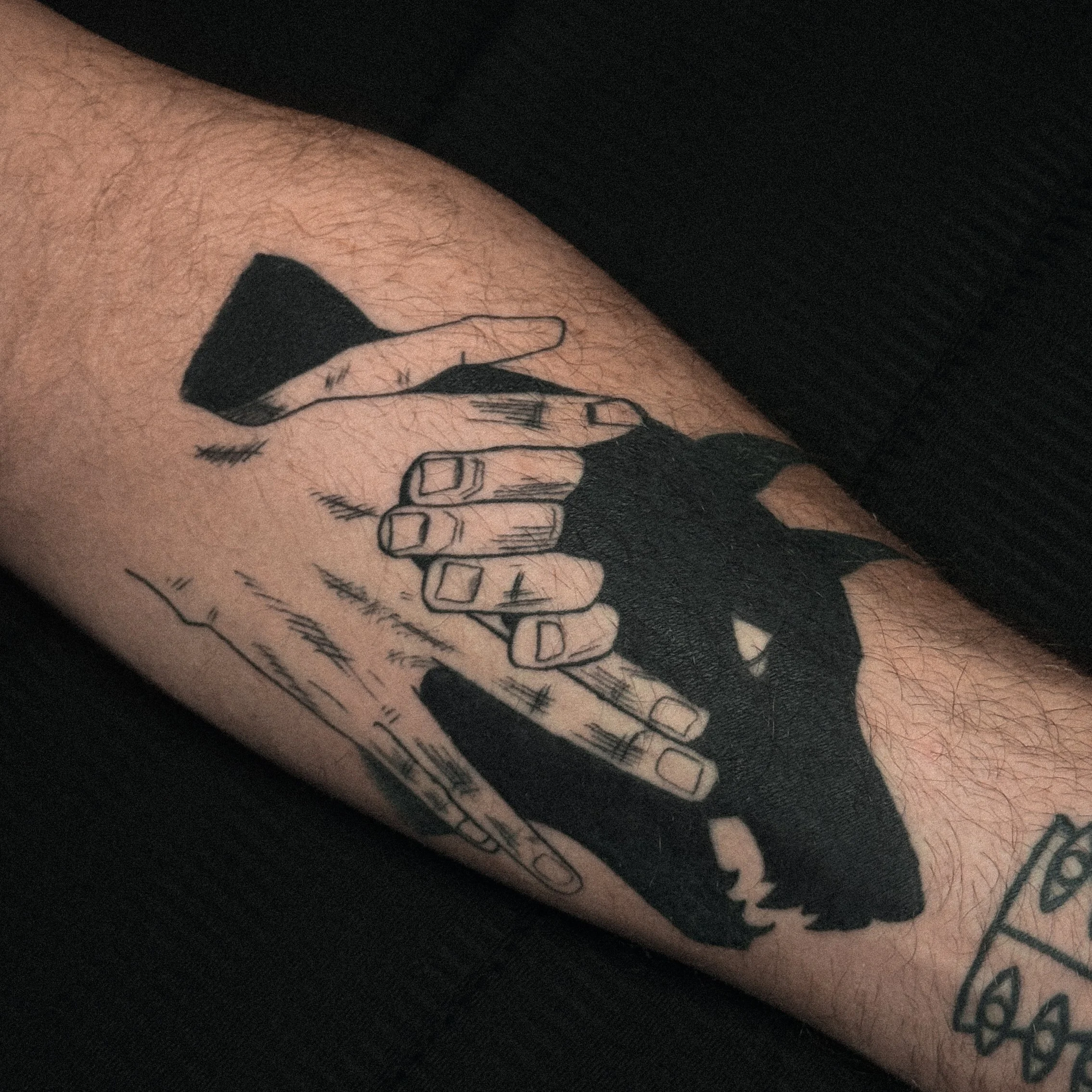 Tattoo of two hands holding each other, outlined in black ink on a person's forearm.