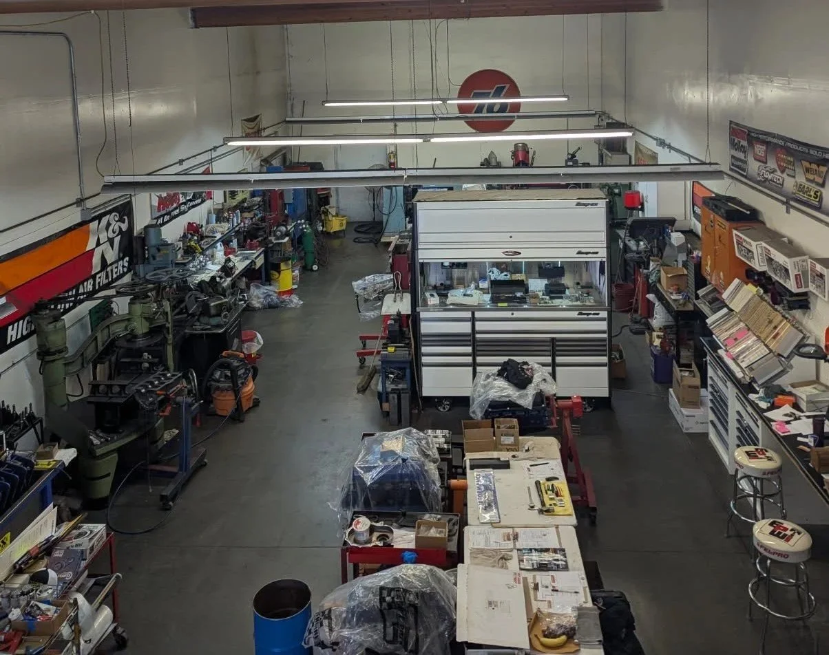 View of Rooster Machine shop floor with various tools, equipment, and parts organized on workbenches and shelves.