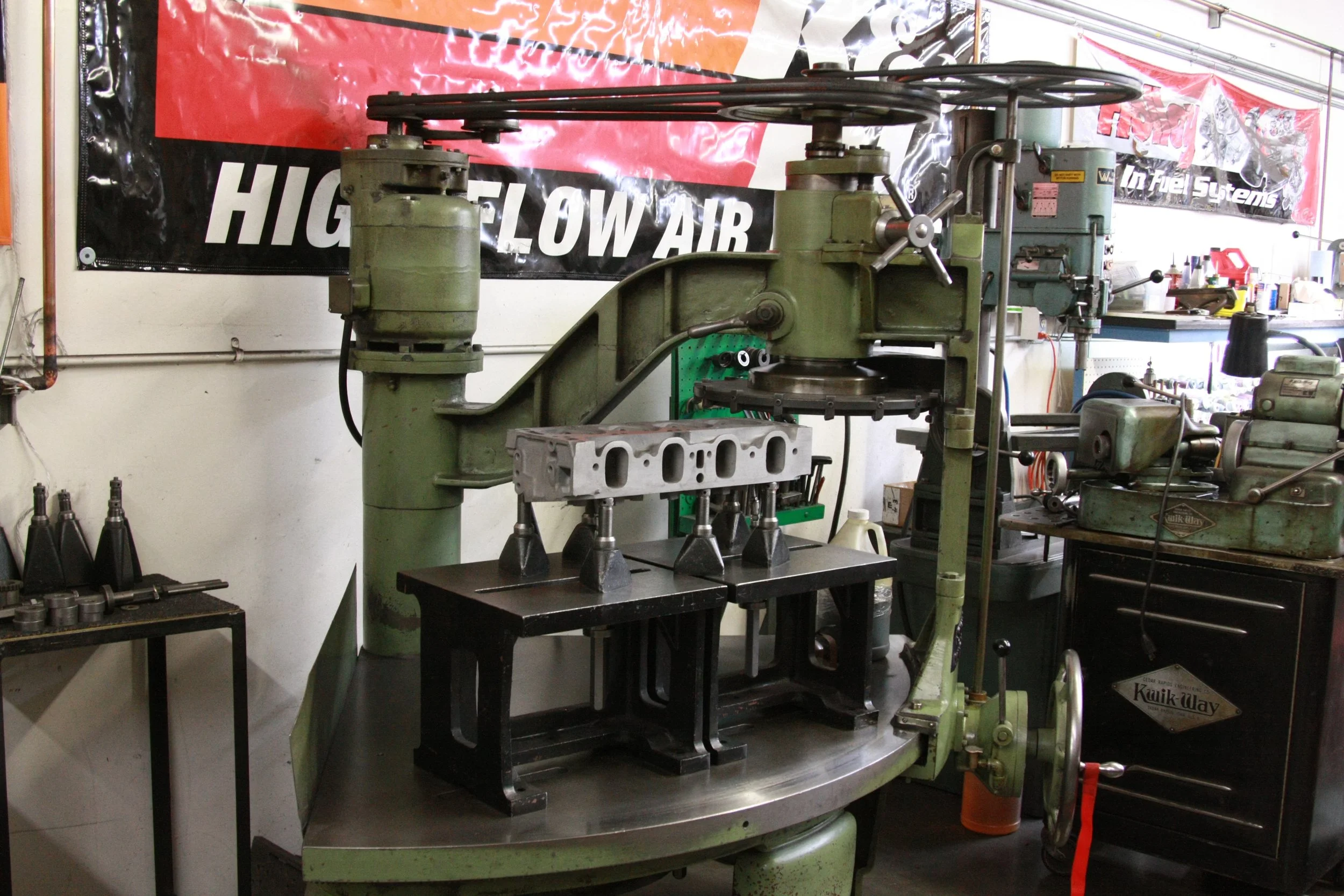 A large, old green industrial machine in a garage or workshop, with various tools and equipment around it, and banners on the wall.