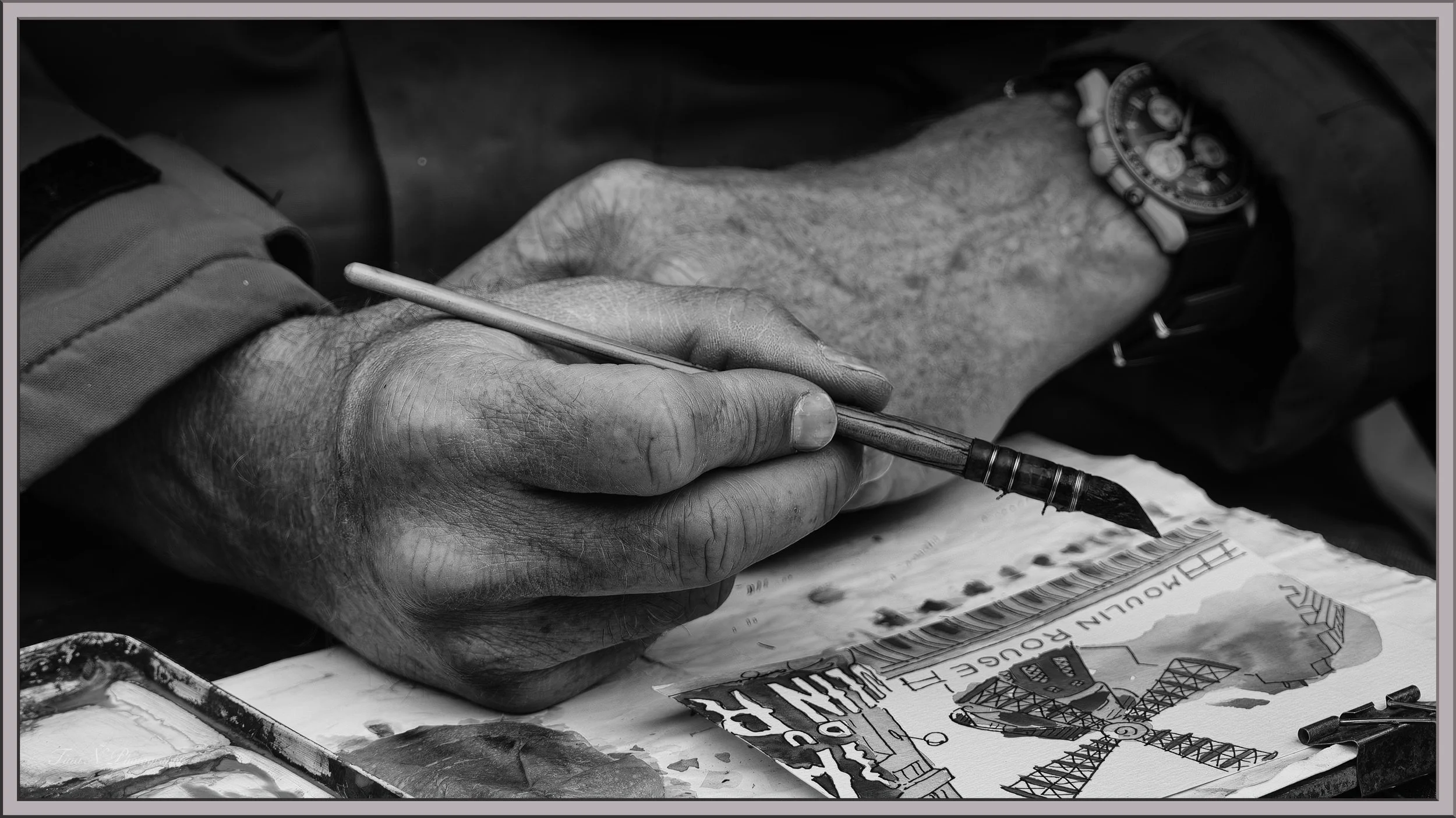 Close-up of an elderly person's hand holding a pen and drawing on a sketchbook, with a wristwatch visible, in black and white.