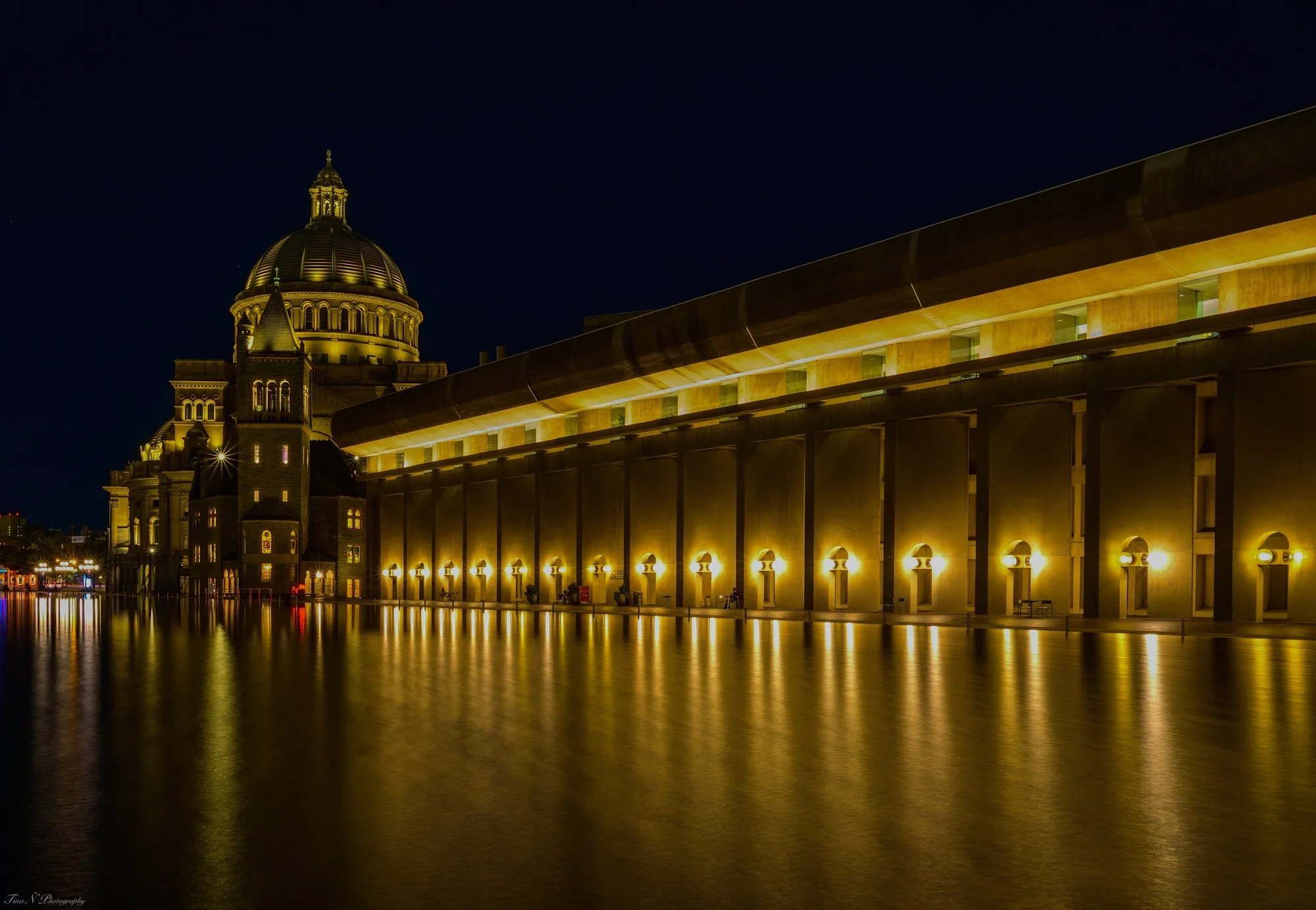 The Christians Center in Boston. Night view of a large, illuminated building with a prominent gold dome and a reflecting body of water in the foreground.