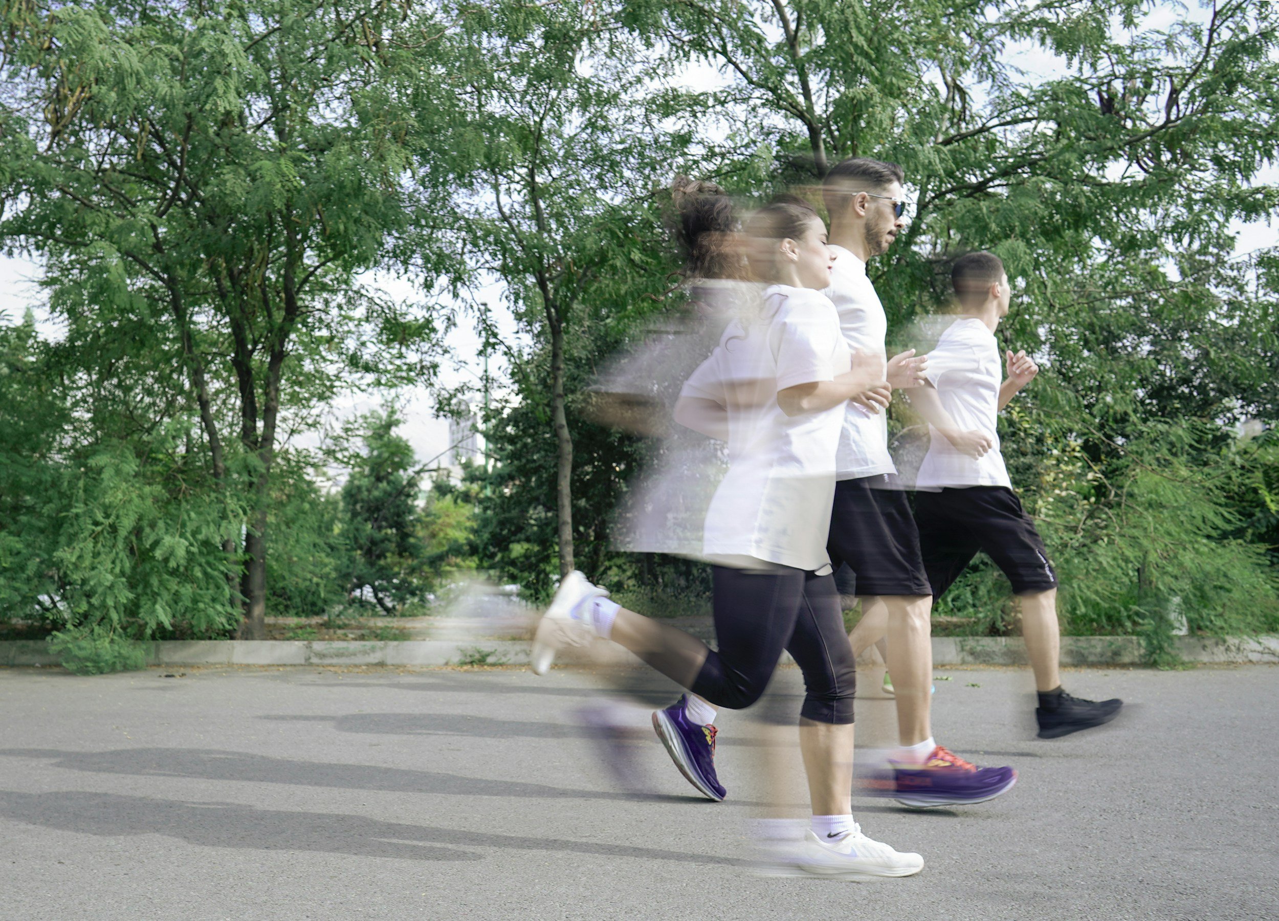 People running outdoors on a paved path with green trees in the background, captured in motion blur.