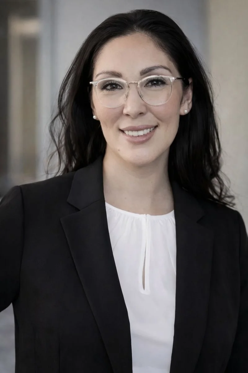A woman with dark hair wearing glasses, a black blazer, and a white blouse, smiling at the camera.