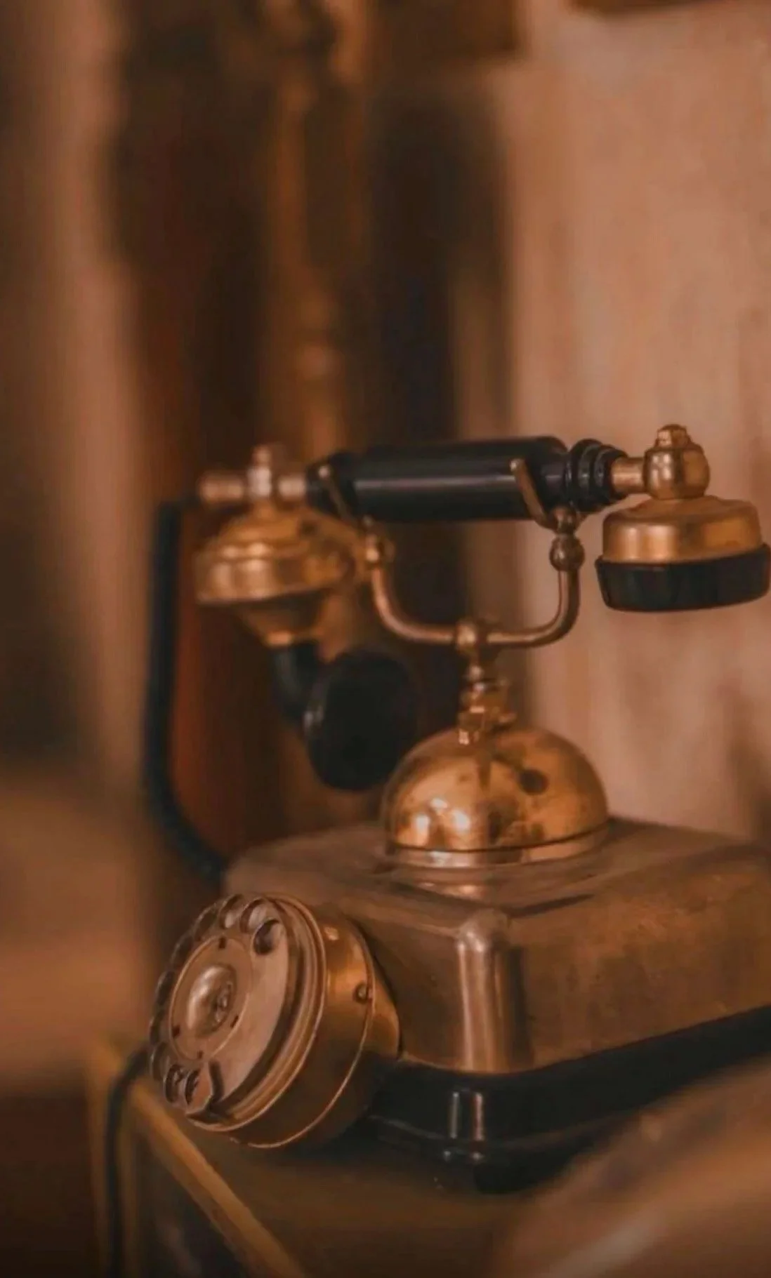 Close-up of a vintage rotary dial telephone with a brass finish on a wooden surface.
