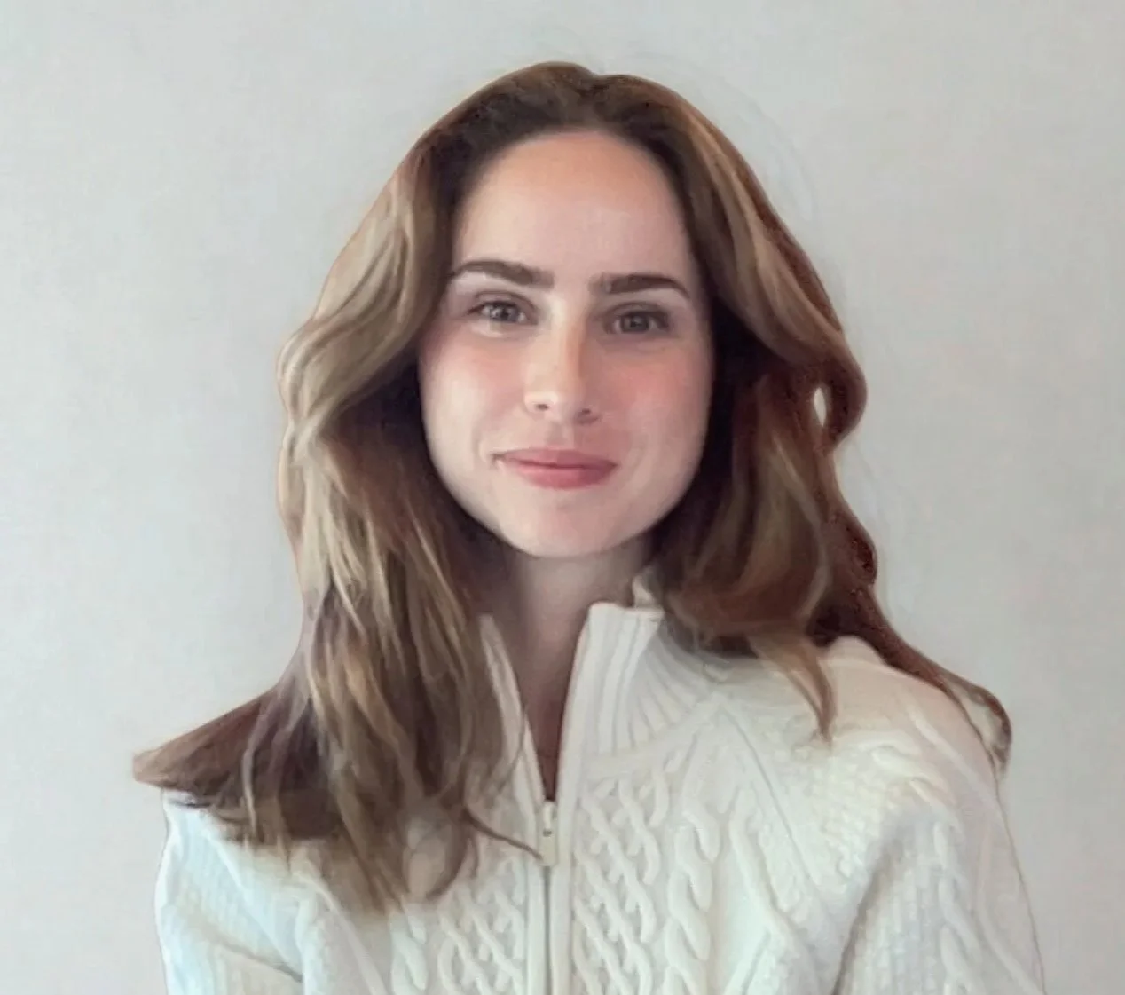 A young woman with wavy brown hair and fair skin smiling softly at the camera against a plain white background.