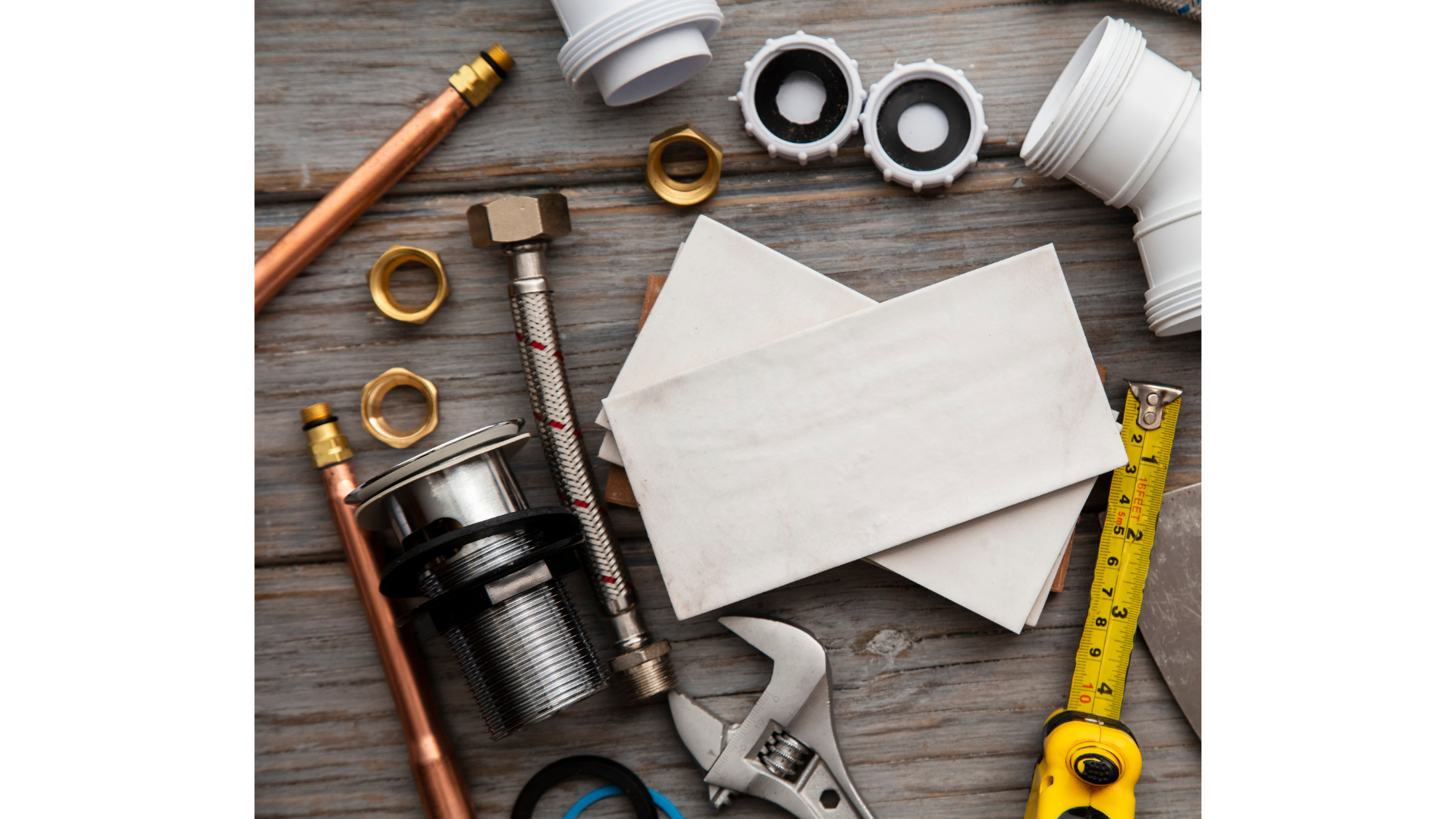 Tools and supplies on a wooden surface, including pipes, fittings, a tape measure, a wrench, and cleaning cloths, likely for plumbing work.