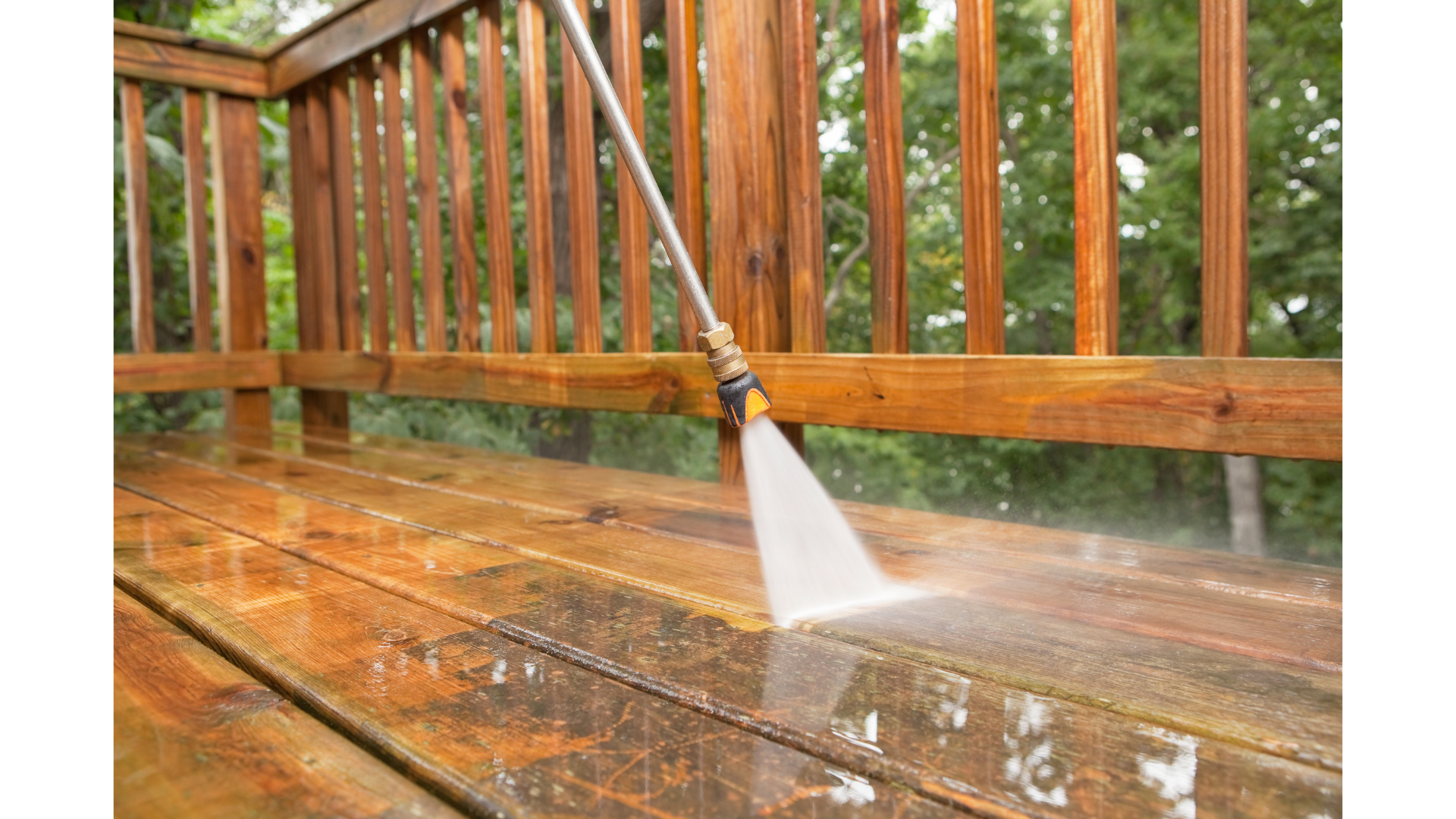 A pressure washer spraying water on a wooden deck, with a wooden railing and trees in the background.