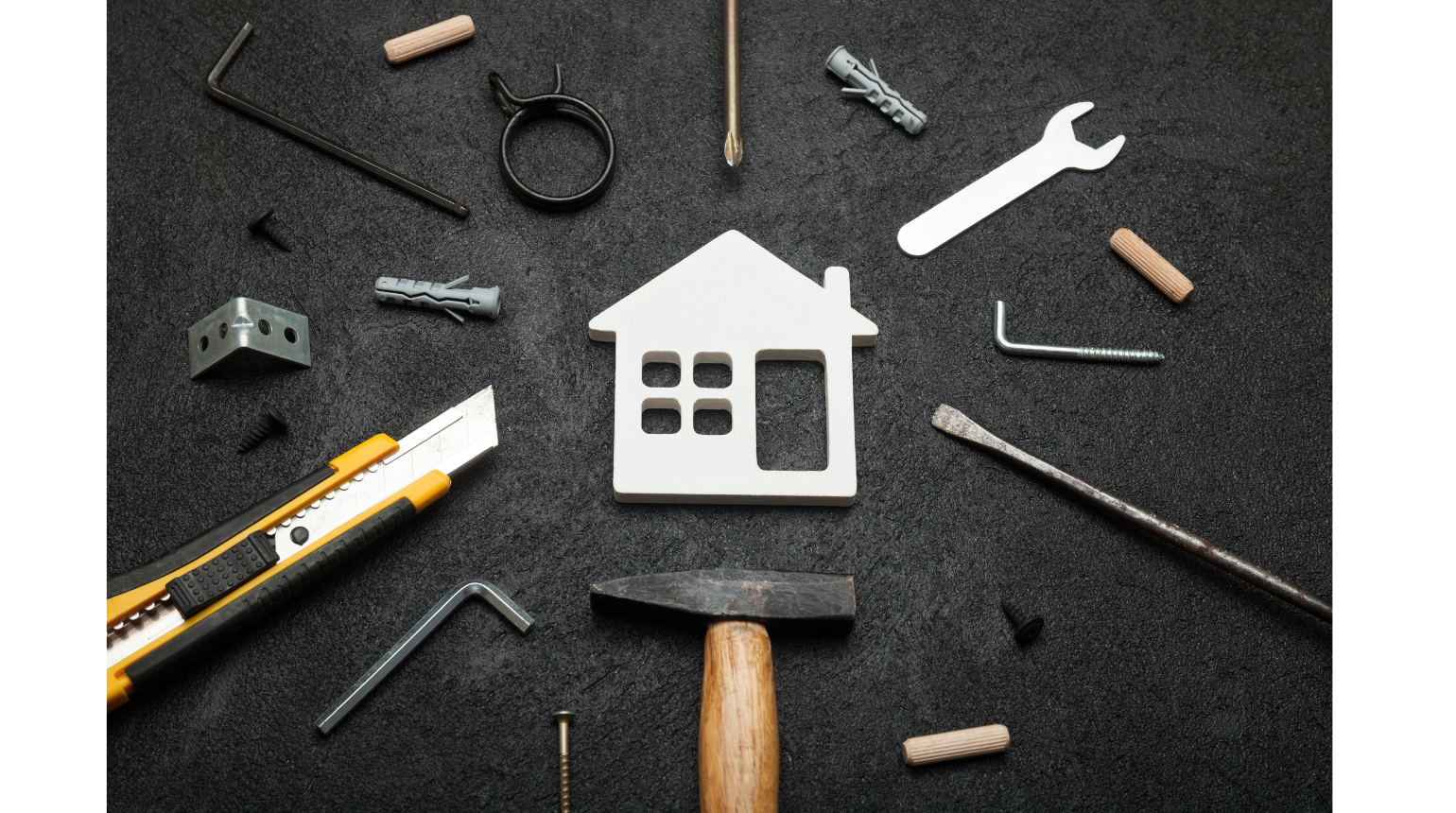 Construction tools and hardware surrounding a white house-shaped cutout on a black surface.