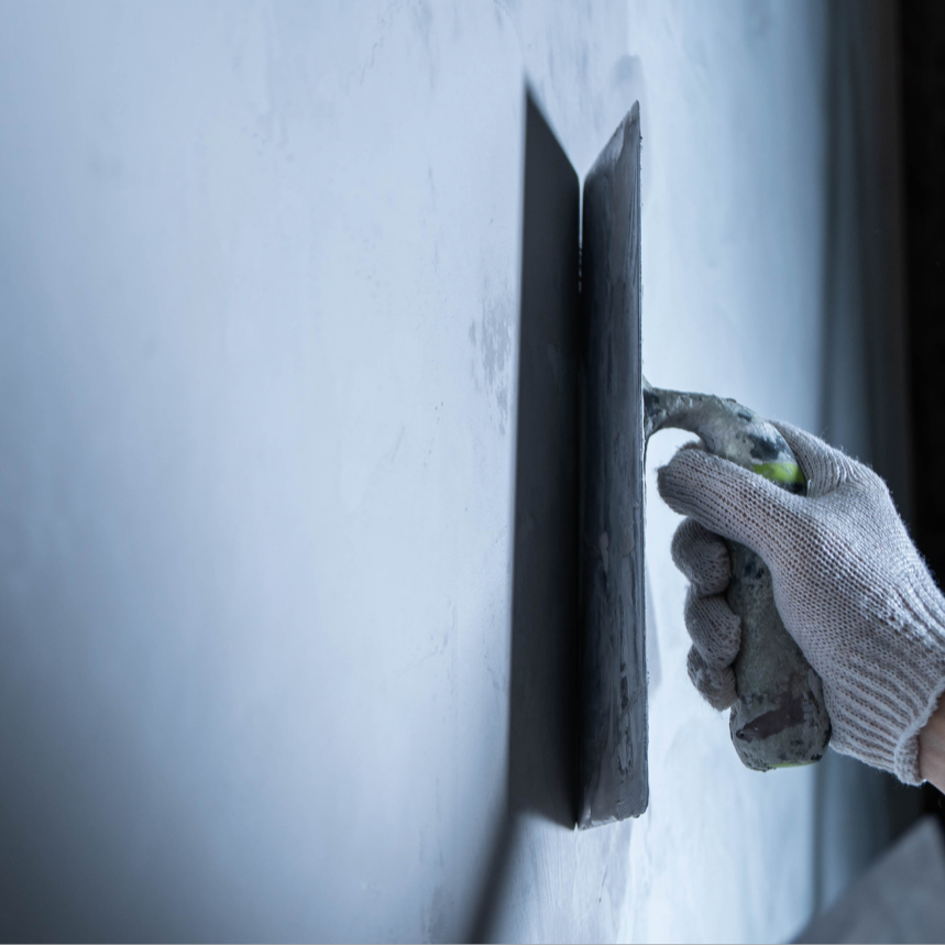 Close-up of a hand in a white work glove holding a trowel, smoothing fresh concrete on a wall or floor.