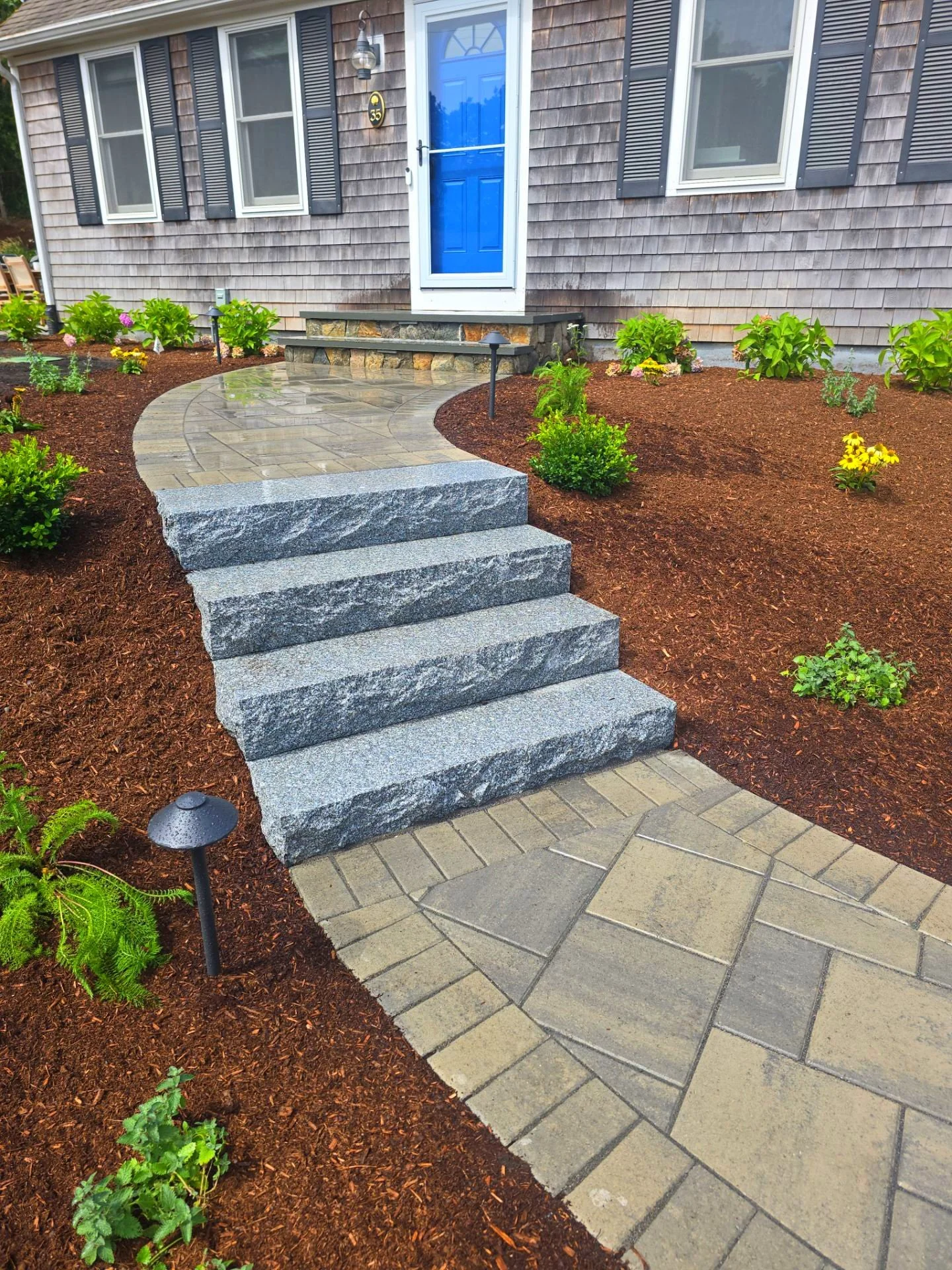 Stone steps leading to a blue front door of a house with a landscaped yard featuring mulch and small plants.