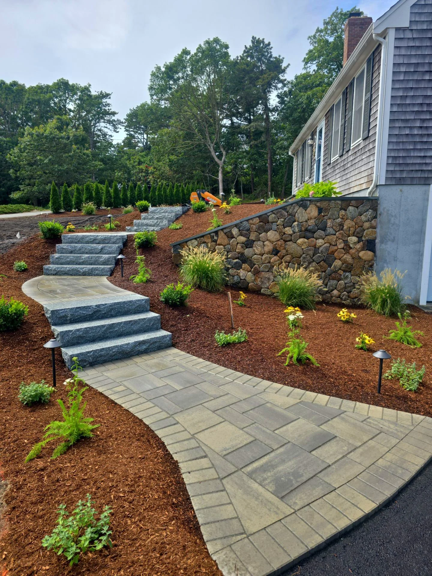  landscaped front yard with stone steps, pathway, mulched flower beds, small bushes, and decorative outdoor lighting.