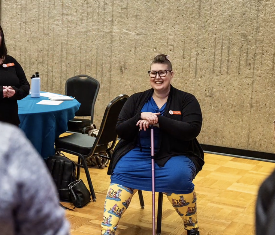 Ursa Scherer sitted smiling at a conference holding her cane.