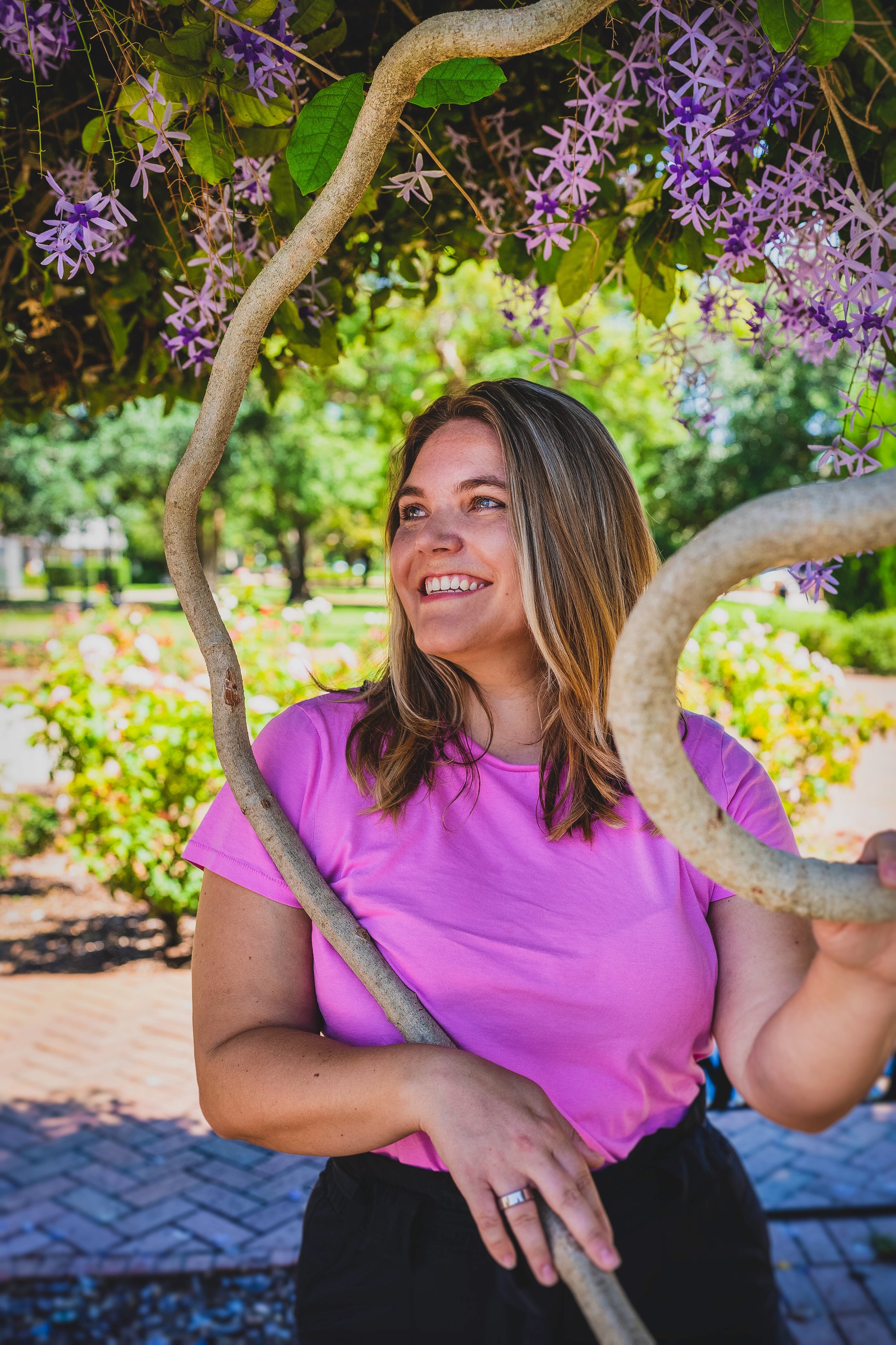 Image of Jess. A landscape design wearing a bright pink shirt sitting under queen's wreath