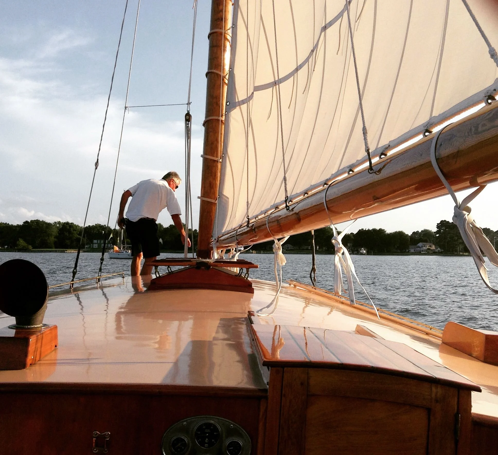 View of the deck on Sail Selina NY yacht, the Selina II, showing wooden craftsmanship, seating area, and sails against the waters near Shelter Island, New York