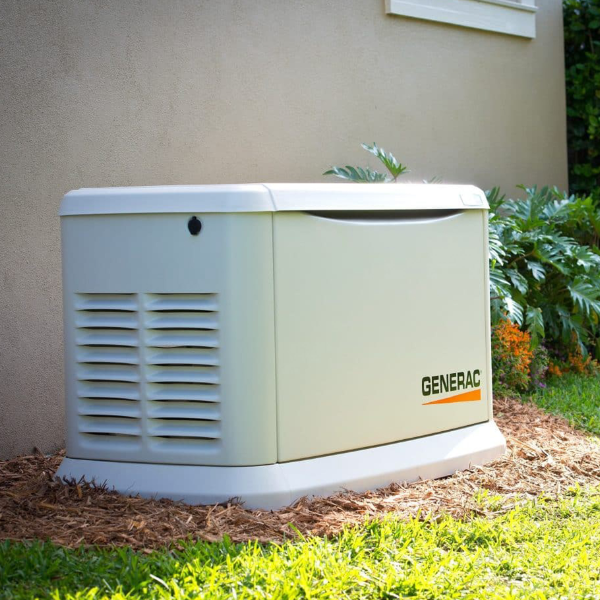 Outside view of a Generac home standby generator installed near a beige wall and surrounded by mulch, grass, and plants.