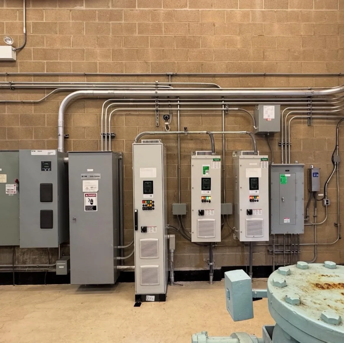 Industrial electrical wiring and control panels mounted on a brick wall in a utility room.