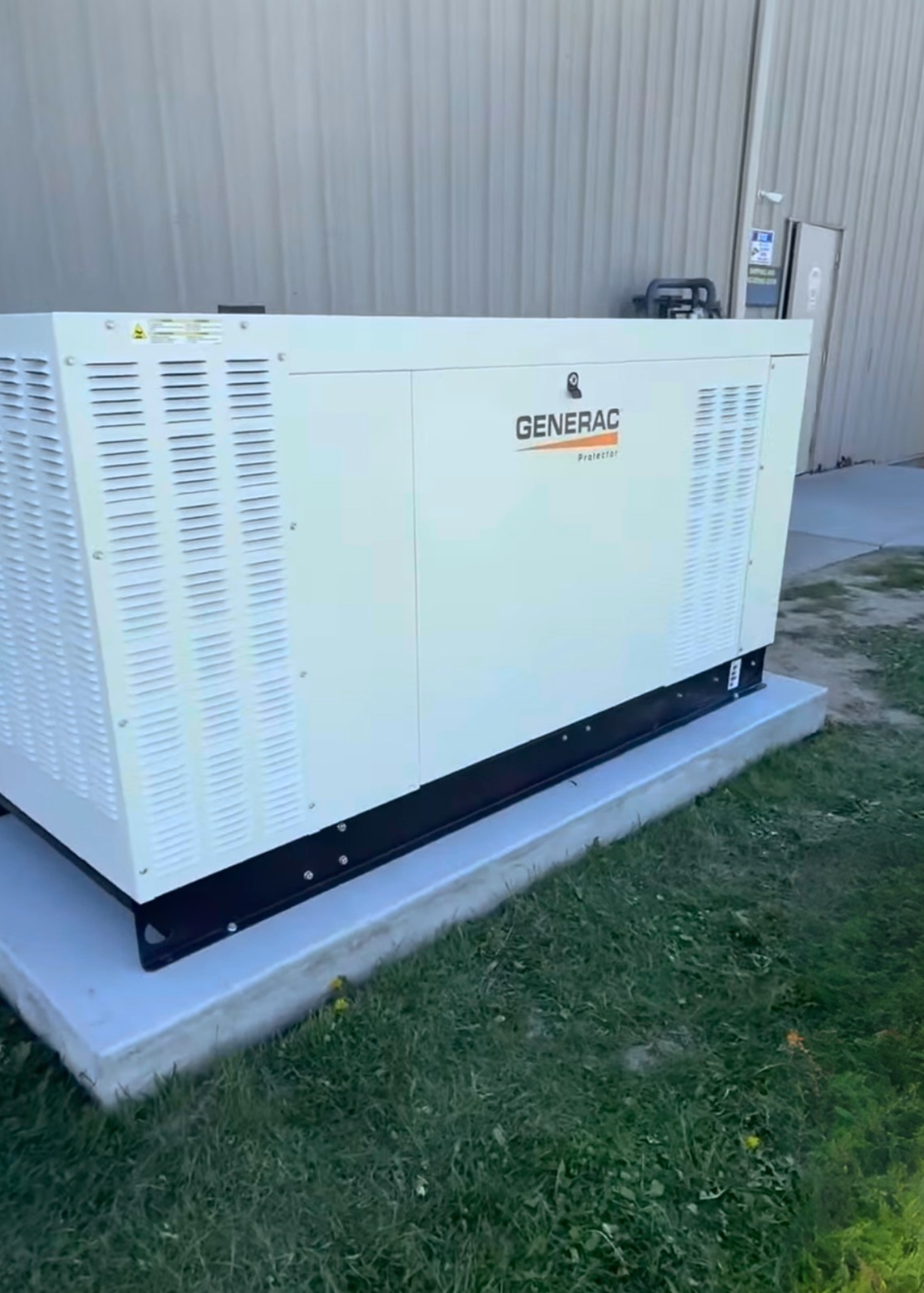 A Generac standby generator installed outdoors on a concrete pad next to a beige building with a metal exterior.