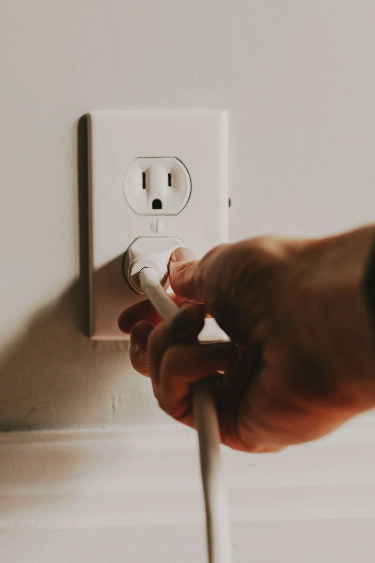 Close up of a hand plugging a power cord into a wall outlet.