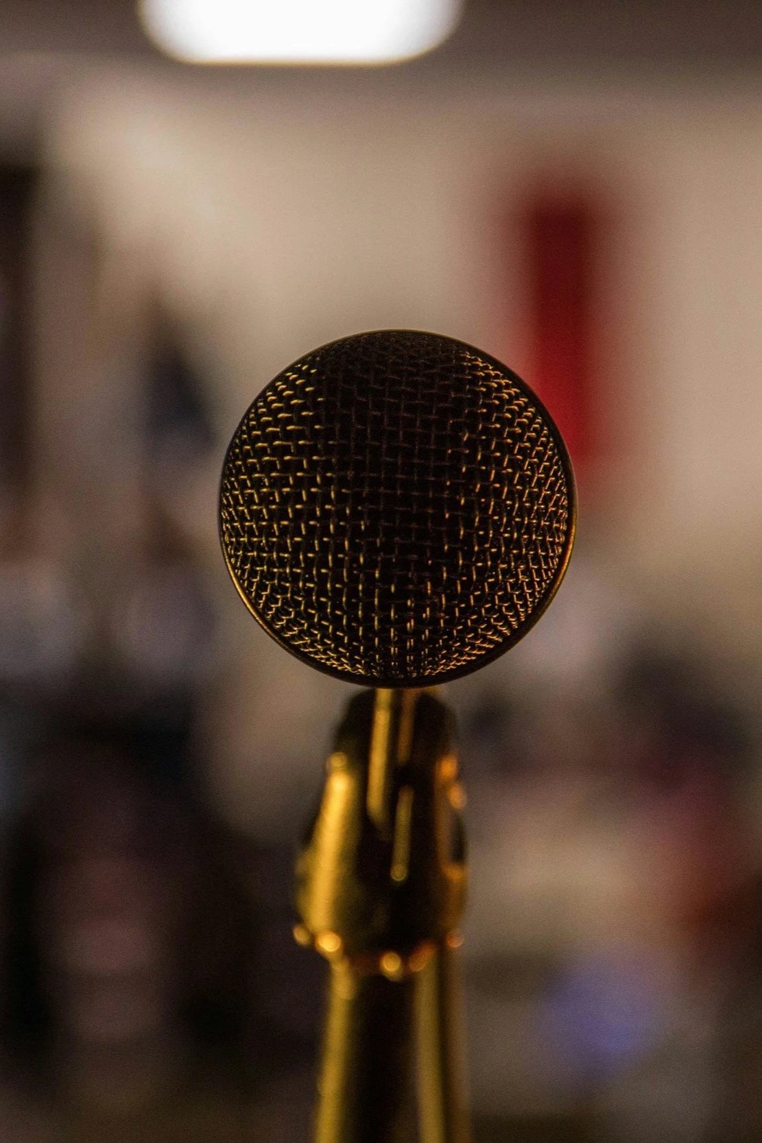 Close-up image of a gold-colored vintage microphone on a stand, with a blurred background.