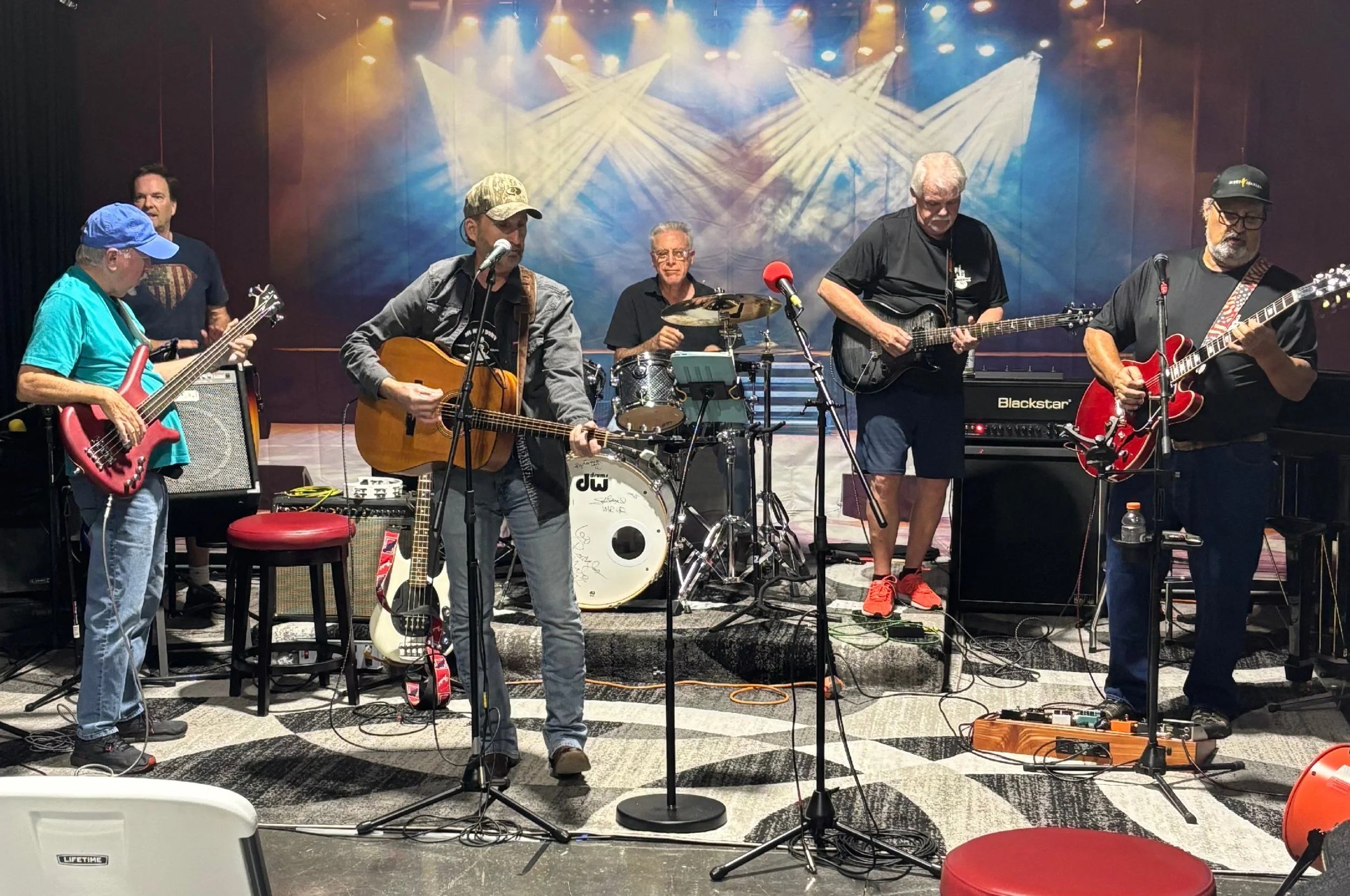 A band performs on a stage with colorful lighting, featuring six musicians with guitars and drums.