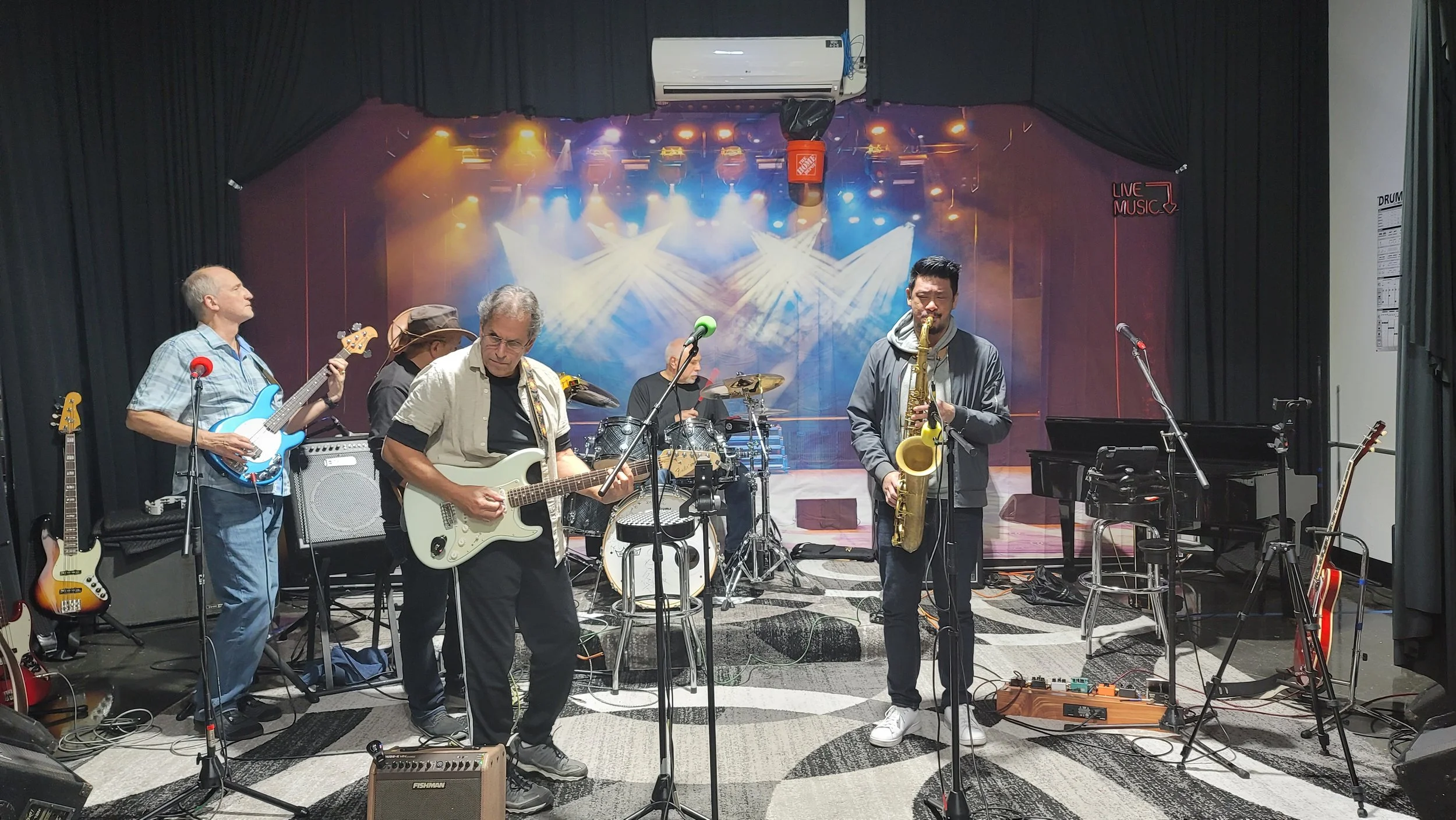 A band of five musicians performing on stage with various instruments, including electric guitar, bass, drums, saxophone, and keyboard, under colorful concert lighting.