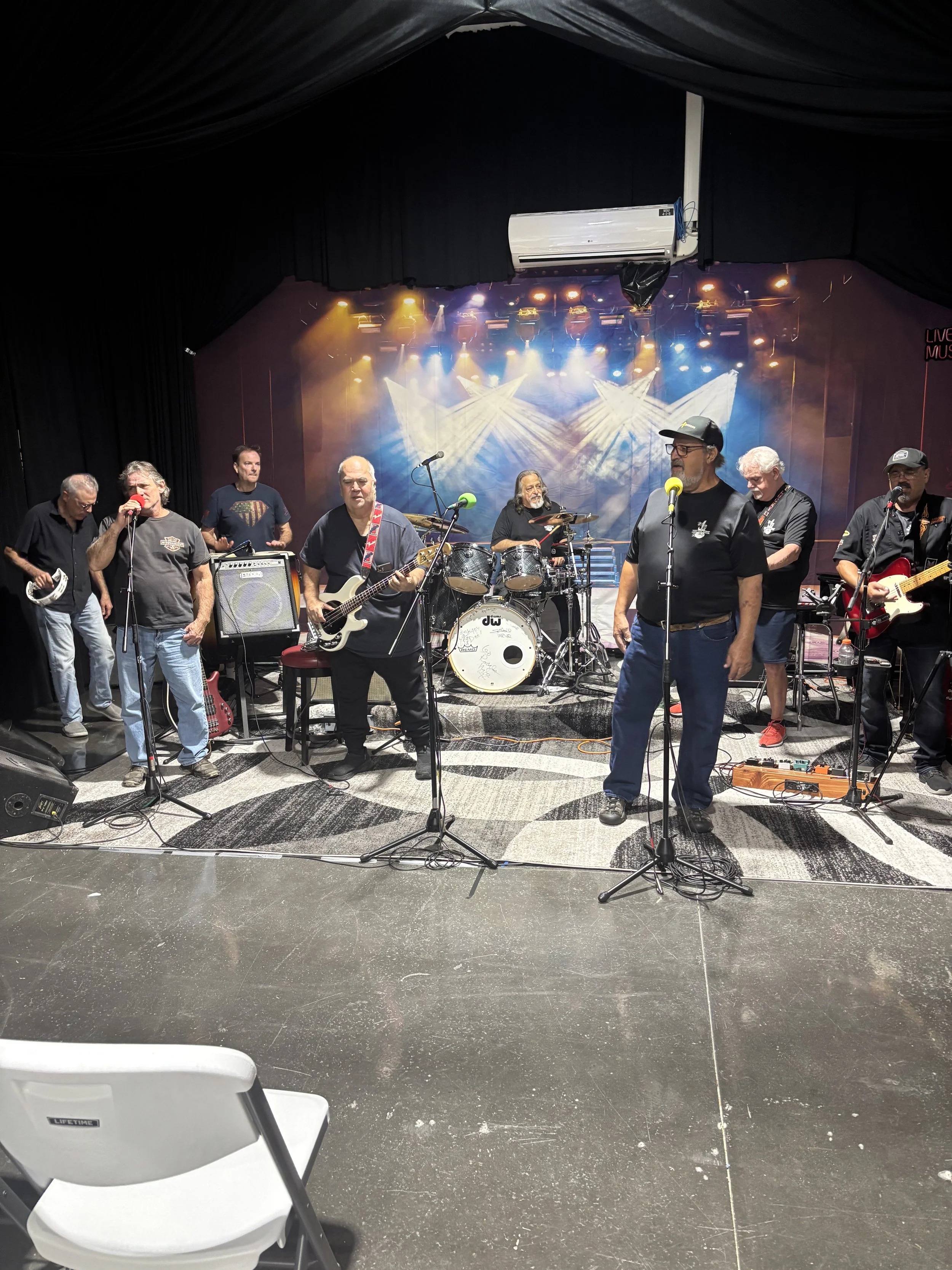 A band performing on stage with various musical instruments, including drums and guitars, under colorful stage lighting.